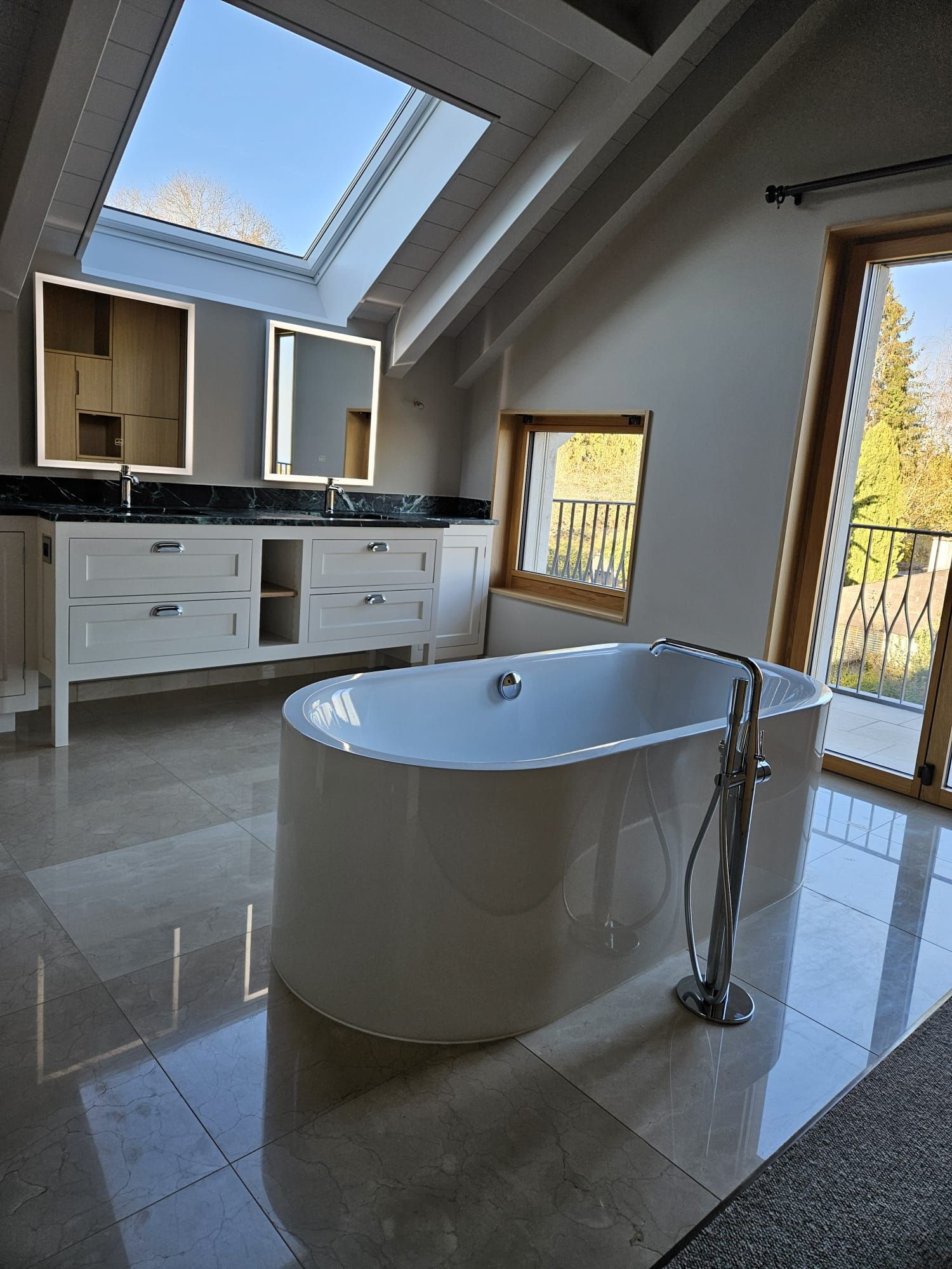 Salle de bains moderne avec baignoire îlot, puits de lumière et meuble-lavabo blanc dans une pièce lumineuse carrelée