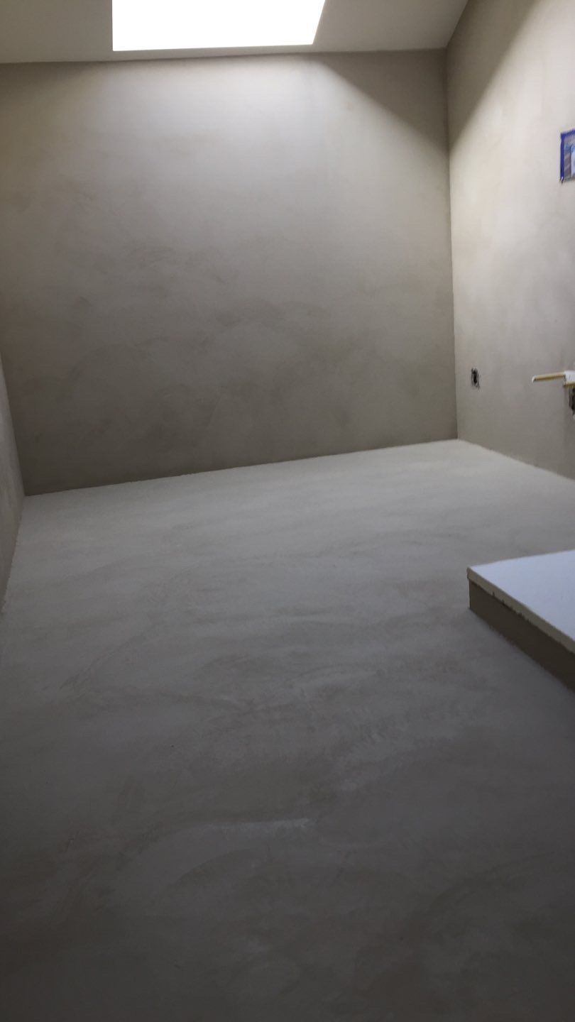 Pièce beige vide avec un puits de lumière, un sol gris lisse et une petite marche dans un coin.