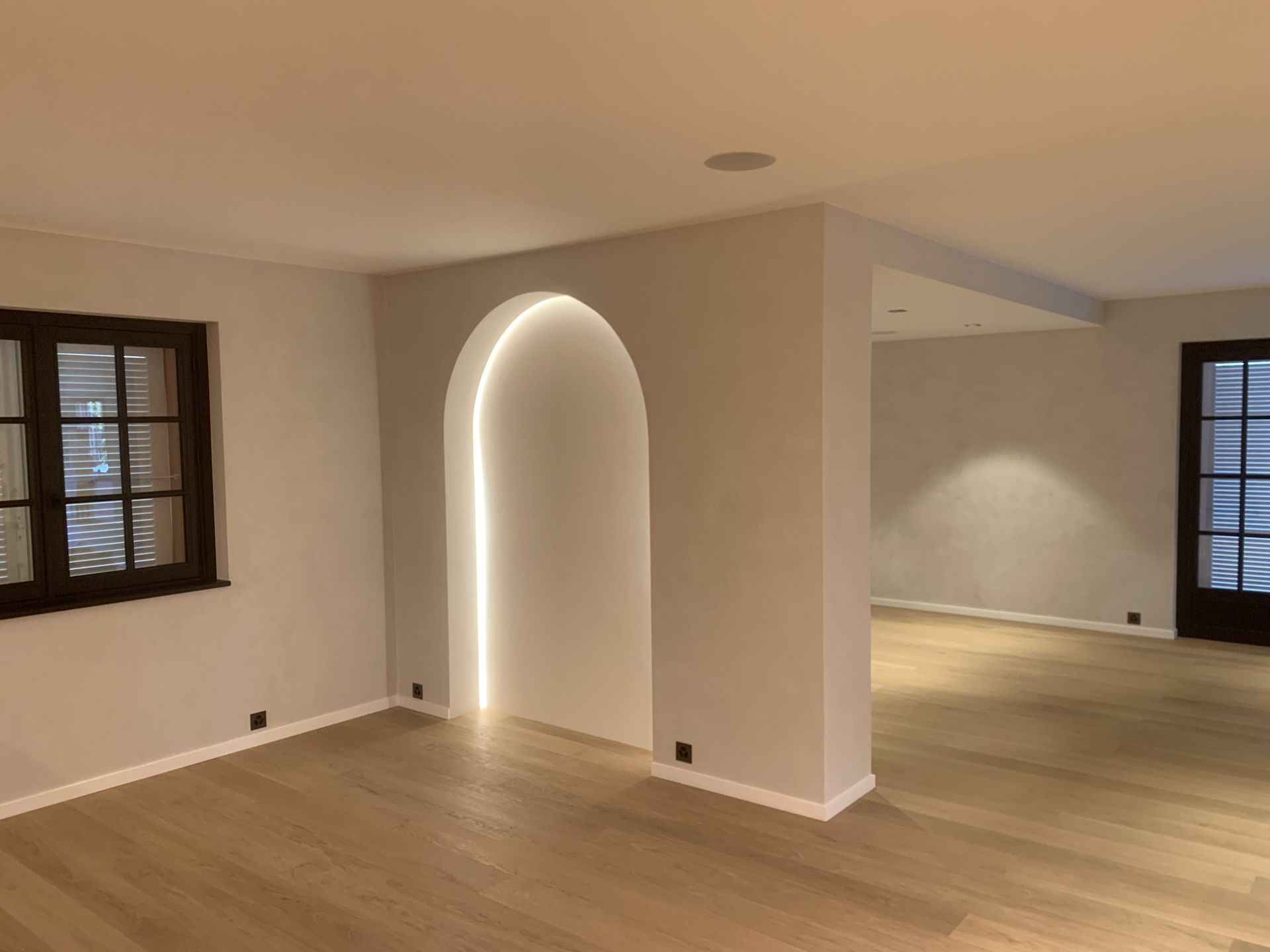 Salon vide avec parquet, alcôve cintrée et fenêtres sur les murs de gauche et de droite.