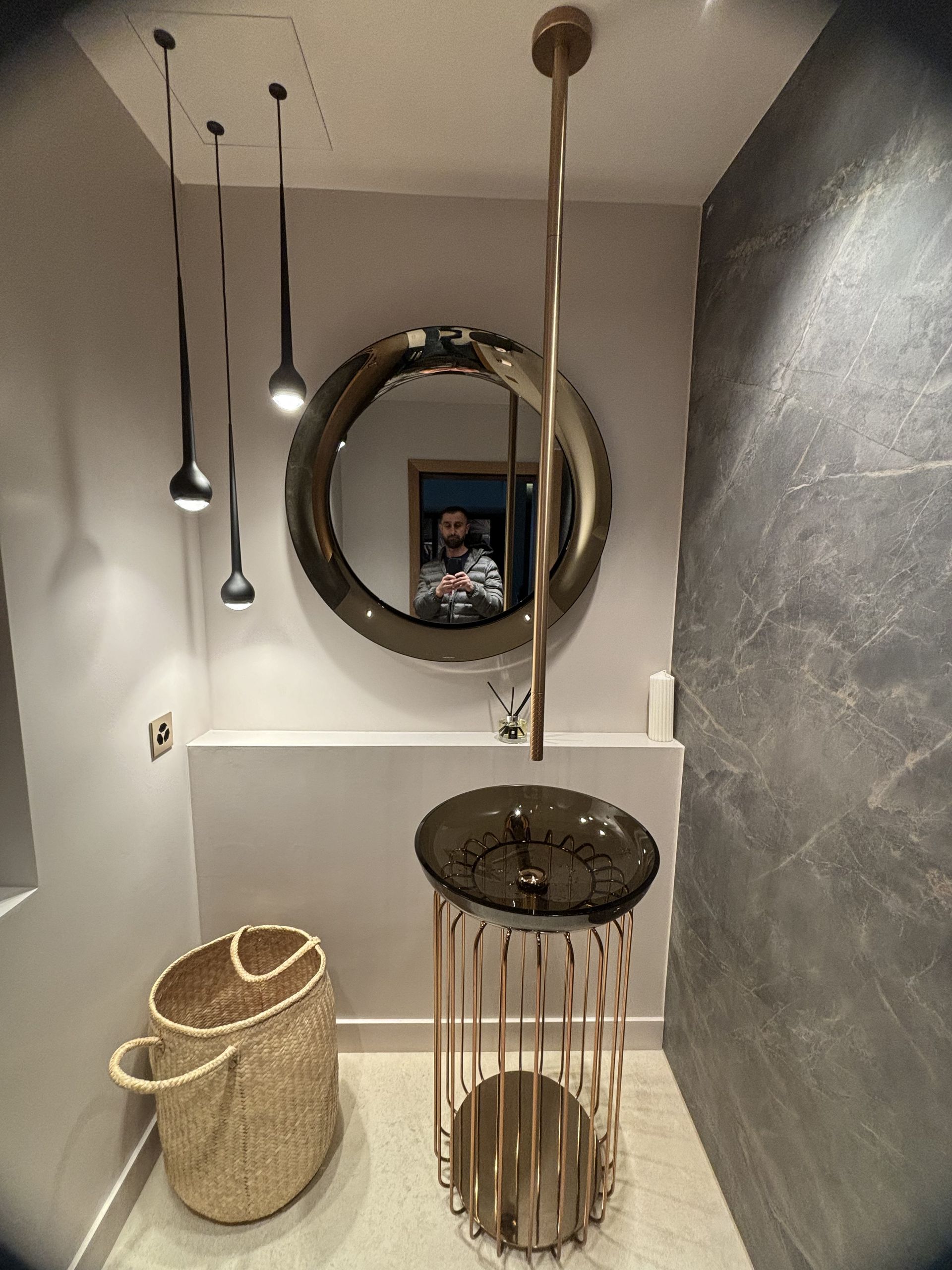 Couloir étroit avec suspensions lumineuses, miroir rond et deux paniers tressés posés au sol.