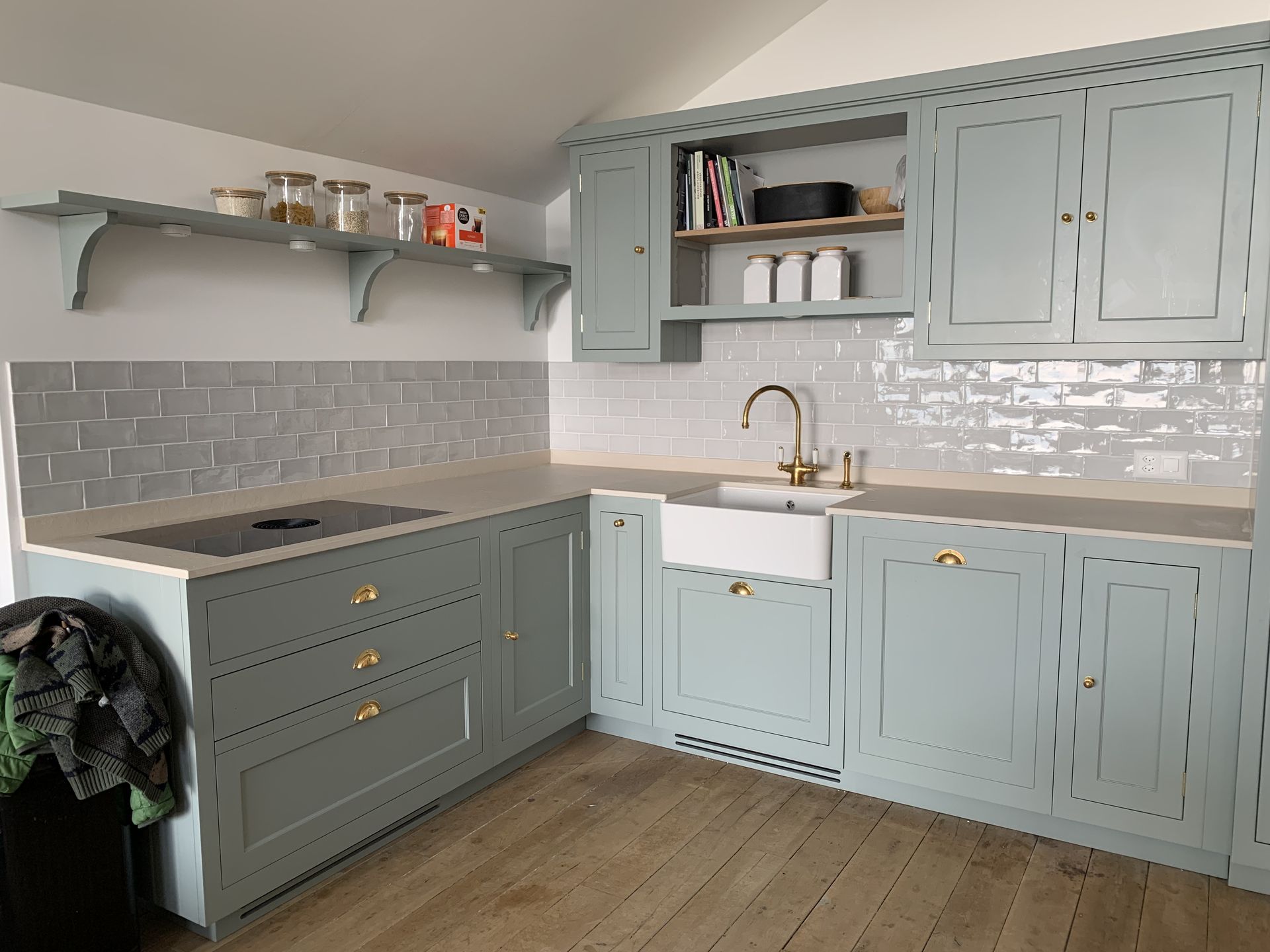 Cuisine bleu clair avec crédence grise, évier blanc, parquet et étagères ouvertes.