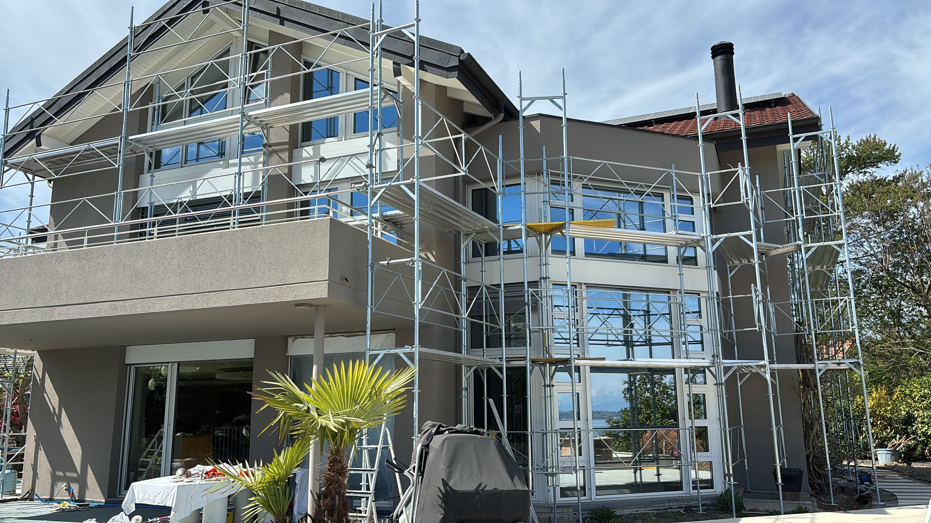 Grande maison moderne en construction, avec échafaudages et charpente apparente autour des fenêtres.