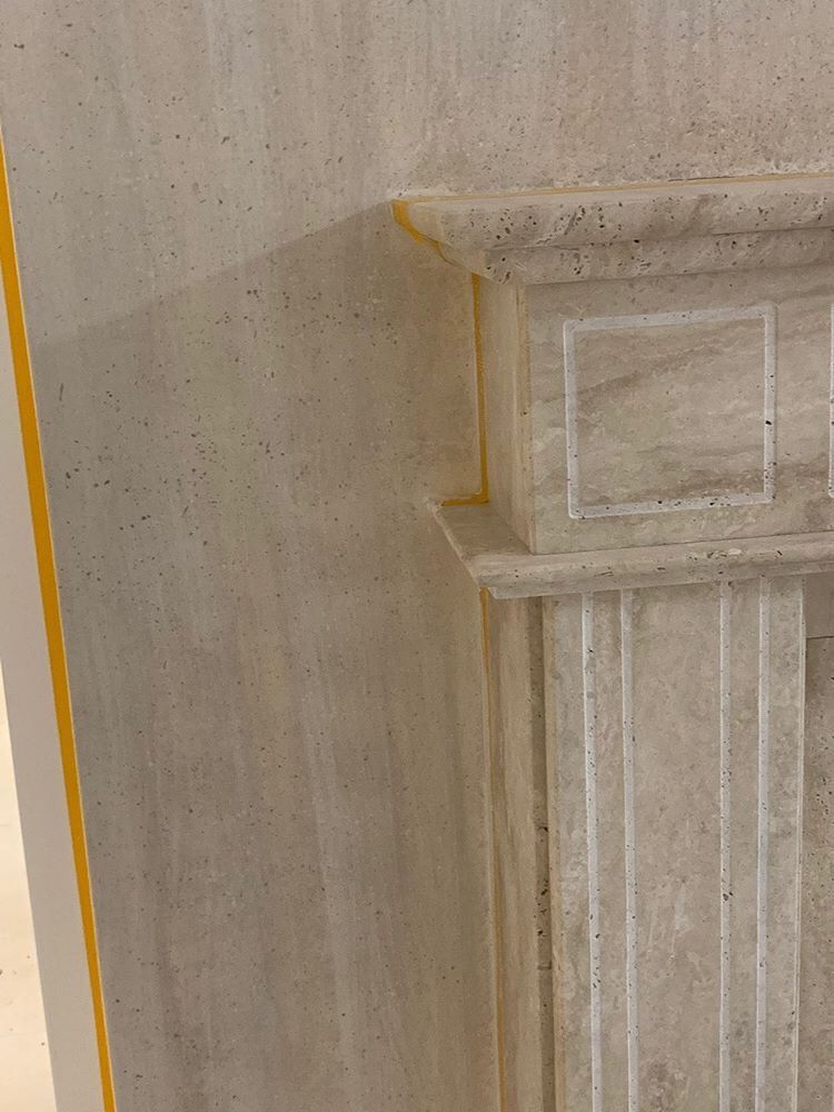 Étagère décorative blanche contre un mur beige texturé, avec des rainures verticales et un bord supérieur sculpté.