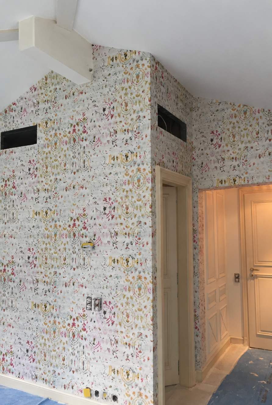 Petite pièce avec papier peint à motifs colorés, deux hautes grilles d'aération et une porte ouverte laissant entrer une lumière chaude.