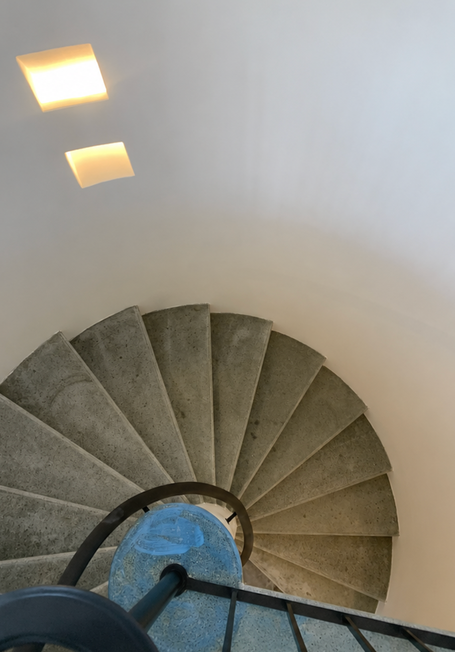 Escalier en colimaçon gris vu du dessus, avec deux plafonniers carrés et une colonne centrale bleue