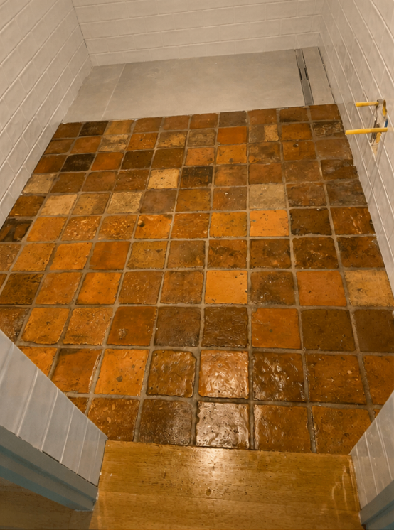 Petite douche carrelée ou sol de salle de bains avec des carreaux carrés brun-orange et un seuil en bois.
