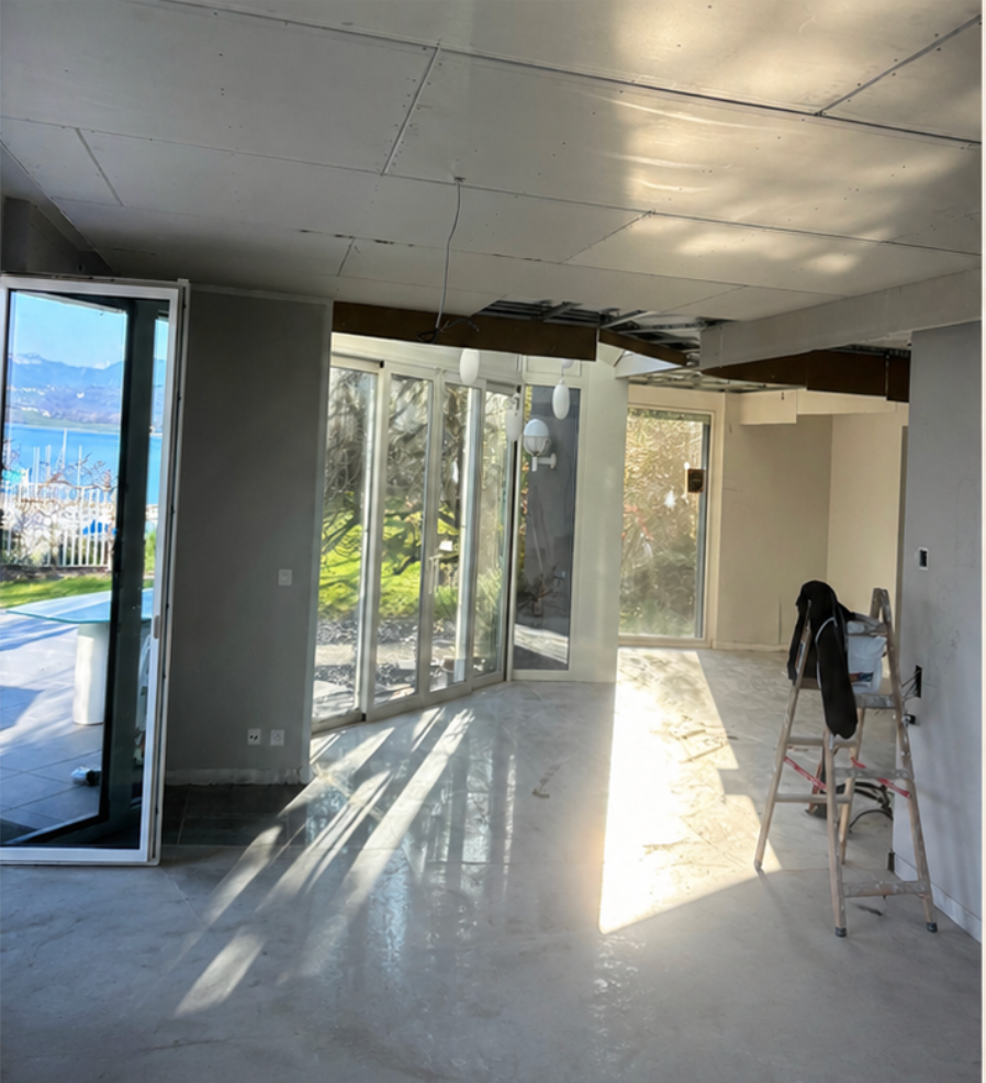 Pièce vide en rénovation avec de grandes fenêtres, une porte ouverte et du soleil sur le sol