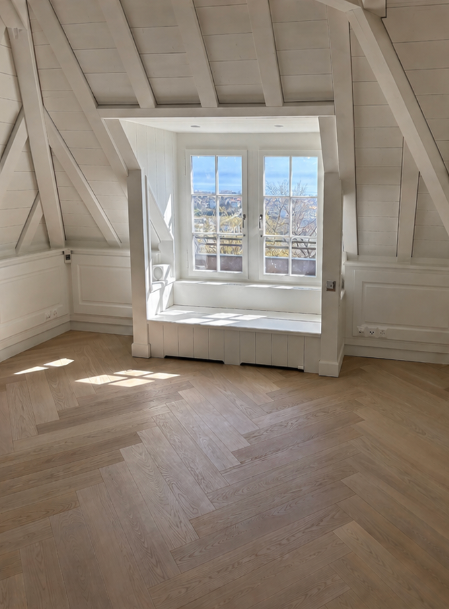 Grenier vide avec poutres blanches, parquet et banquette lumineuse près de la fenêtre donnant sur les toits et le ciel