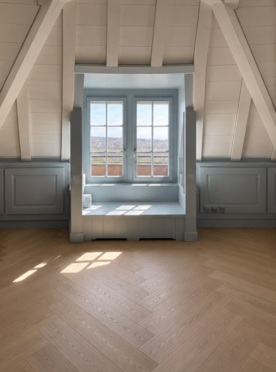 Chambre mansardée lumineuse avec une fenêtre à cadre bleu et la lumière du soleil sur le parquet.