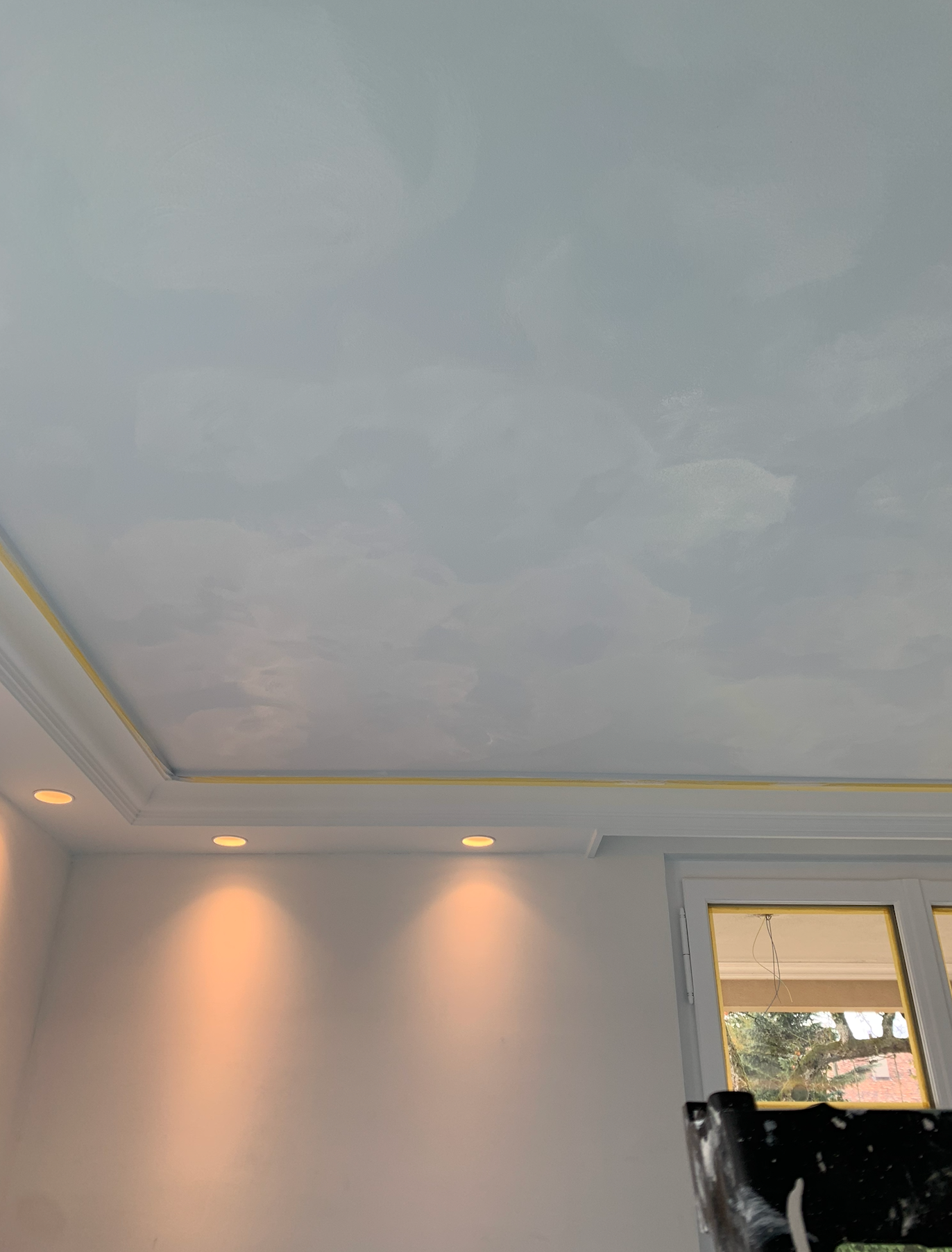 Plafond du salon avec spots encastrés, éclairage mural doux et fenêtre avec rideaux.