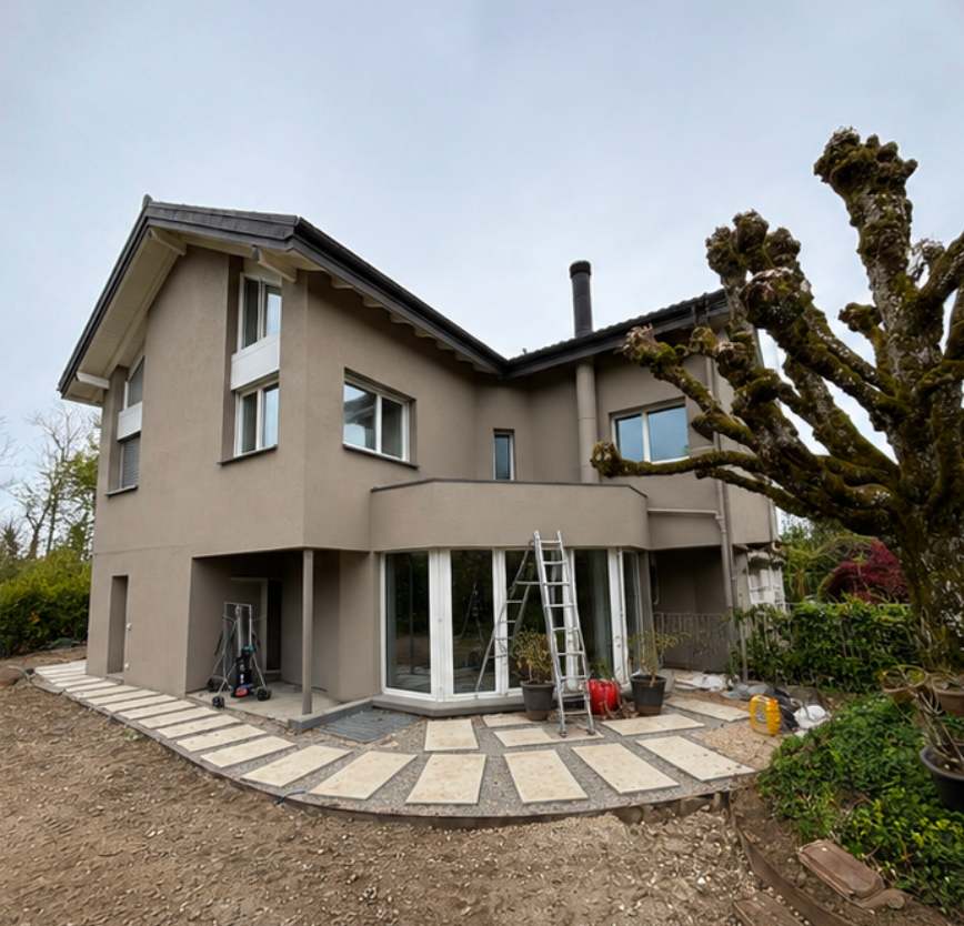 Maison beige à deux étages avec un patio incurvé, une échelle ouverte et un arbre taillé dans le jardin
