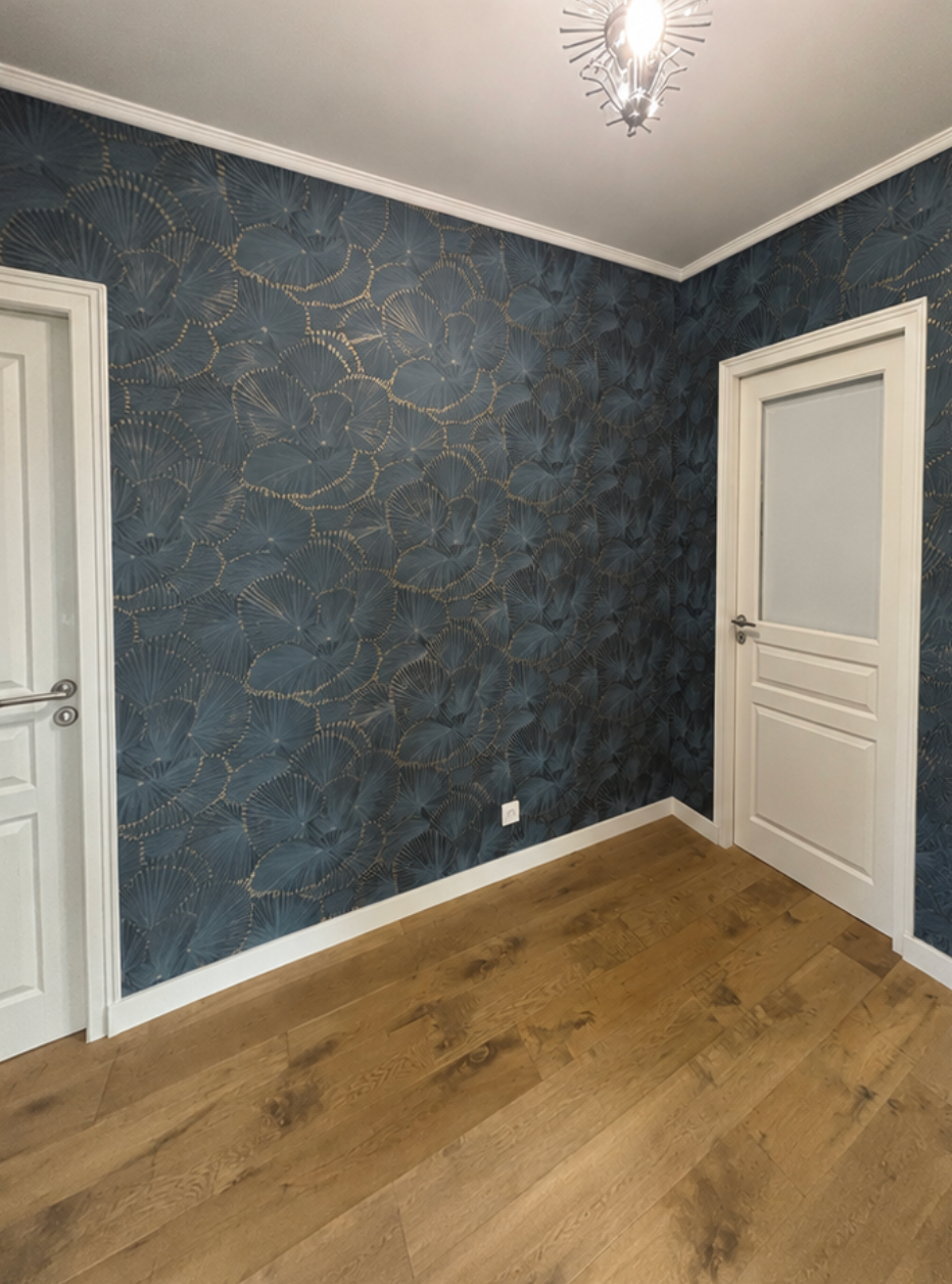 Pièce vide avec papier peint texturé bleu, parquet clair, portes blanches et plafonnier.
