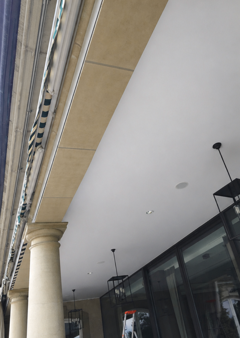 Allée extérieure couverte avec colonnes, façades de magasins en verre et éclairage au plafond, à côté d'un bâtiment.