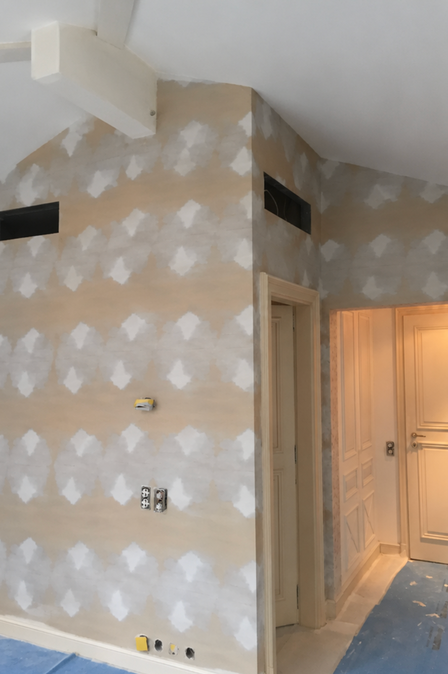 Pièce intérieure en rénovation avec cloisons sèches abîmées, encadrement de porte et lumière orangée provenant d'une pièce adjacente