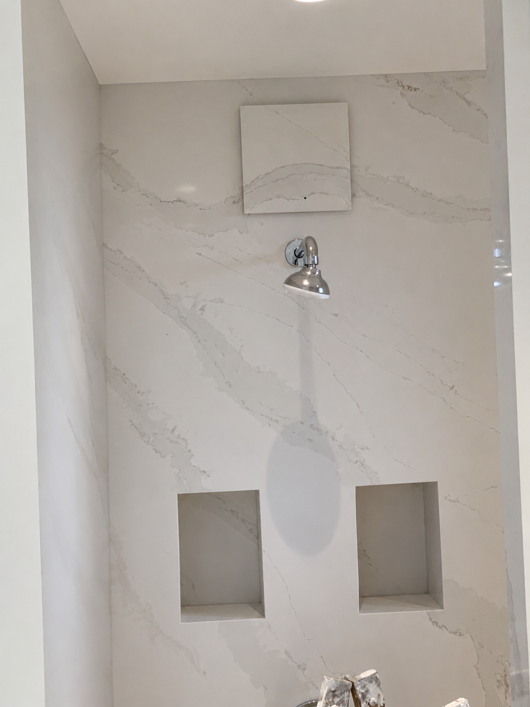 Mur de douche carrelé en blanc avec deux étagères encastrées et une pomme de douche chromée.