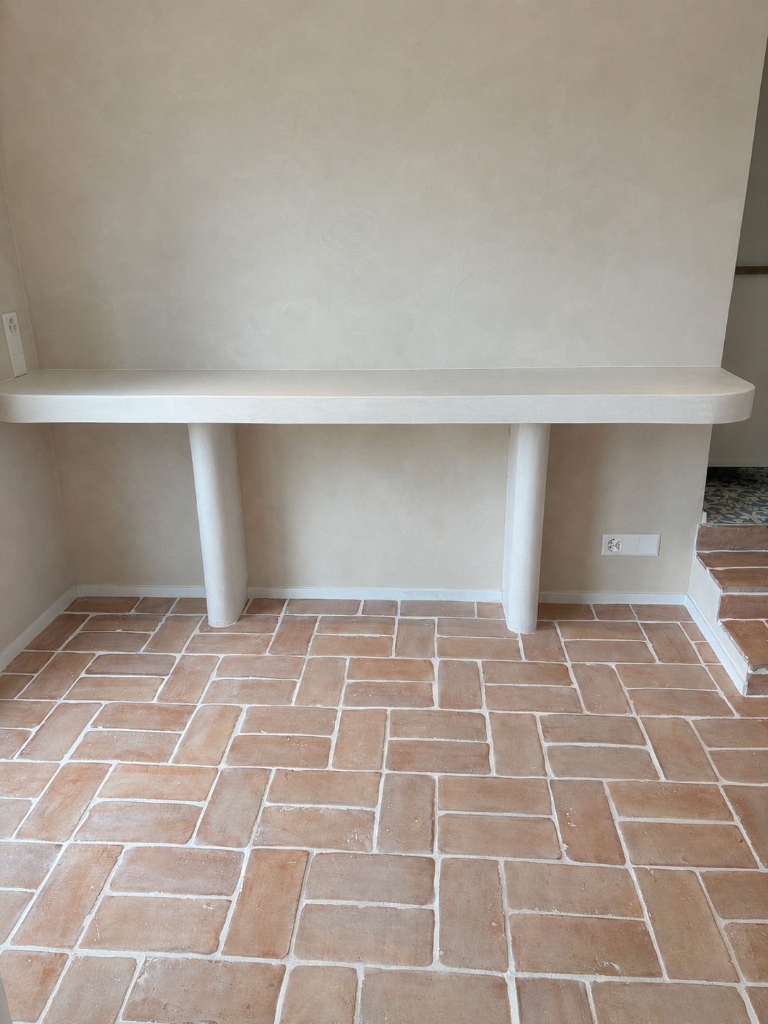 Bureau blanc intégré contre un mur beige au-dessus d'un sol en terre cuite