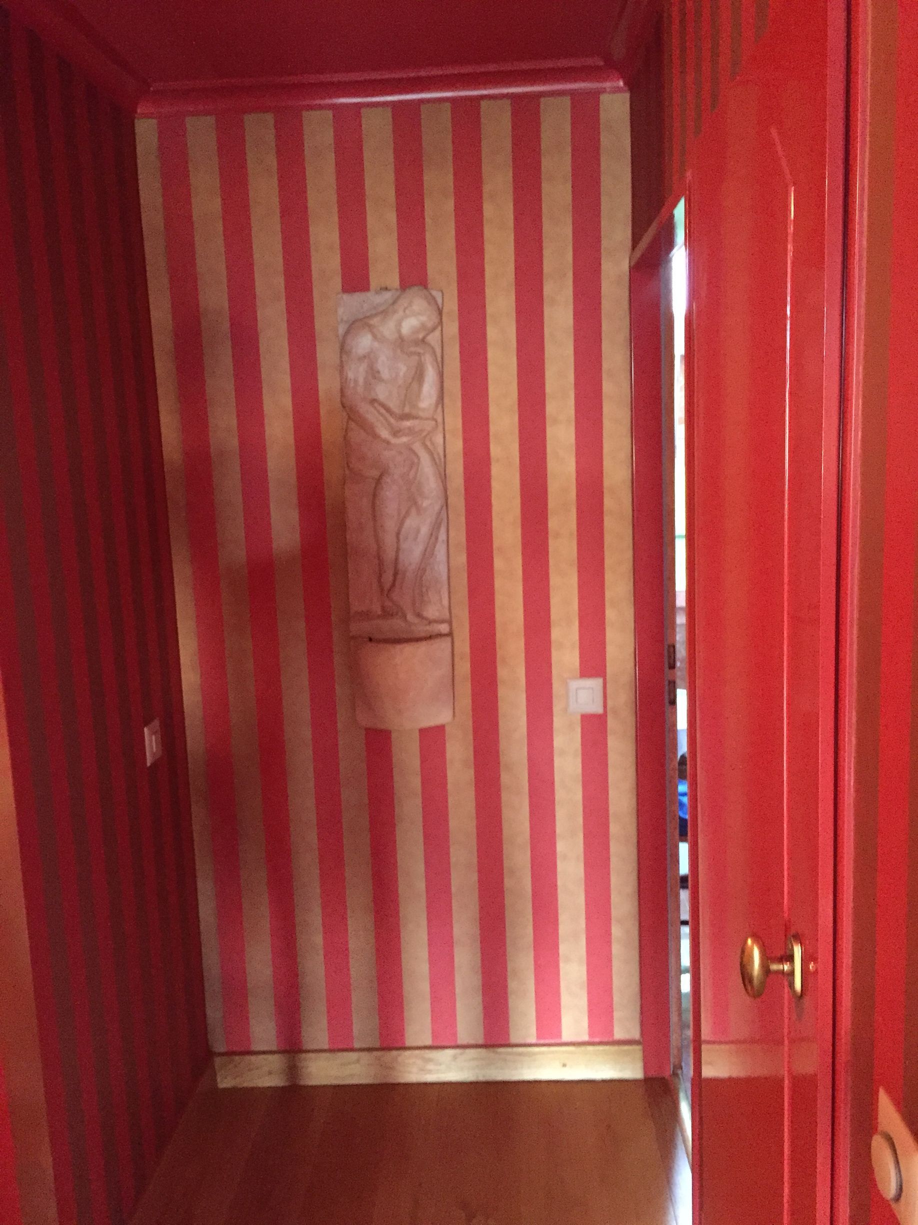 Couloir à rayures rouges avec un bas-relief sculpté et une porte rouge ouverte sur la droite