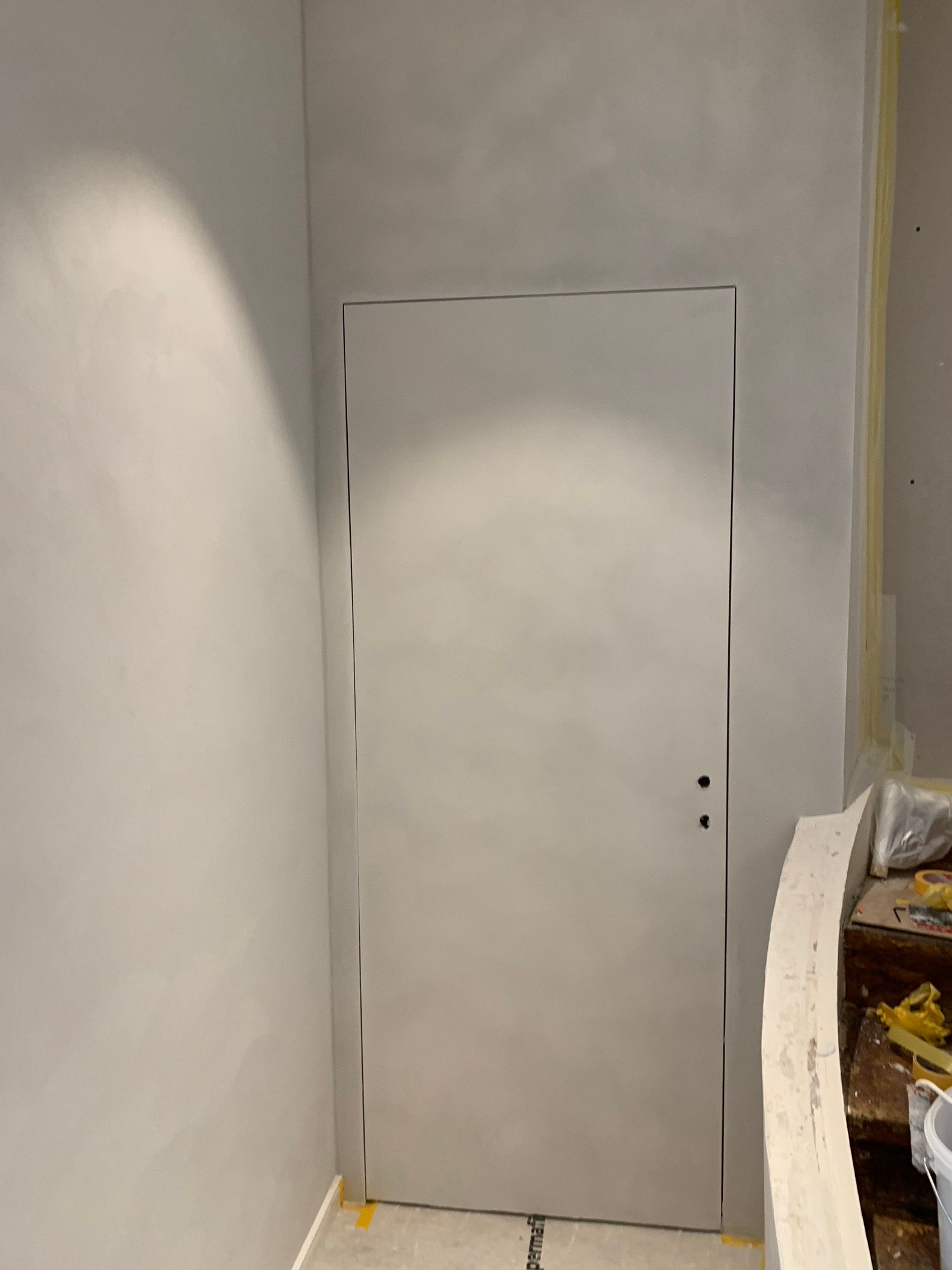 Porte intérieure blanche dans un couloir nu, avec une petite étagère sur le côté droit.