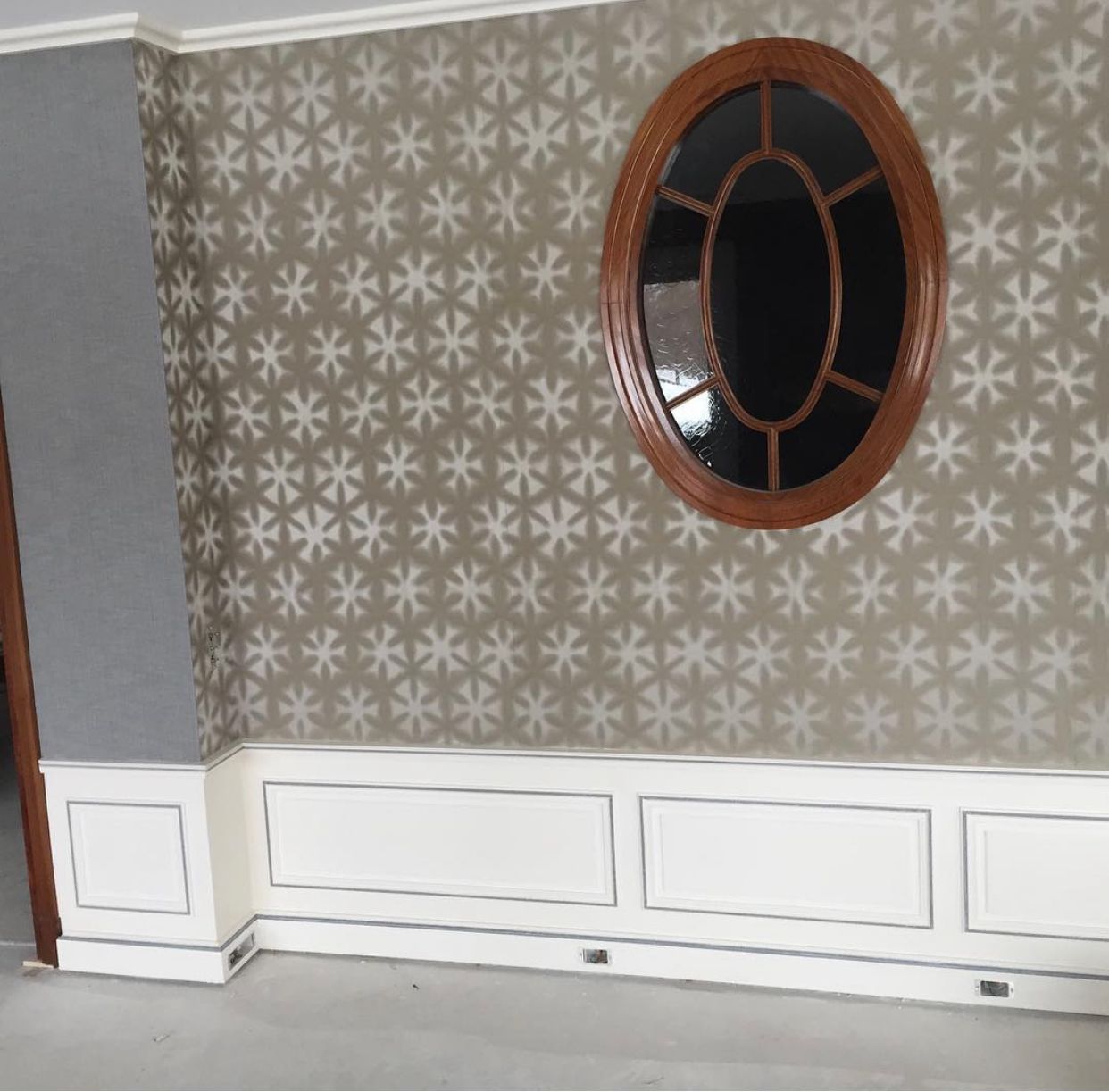 Mur intérieur décoratif avec papier peint à motifs floraux, lambris blanc et miroir rond à cadre en bois.