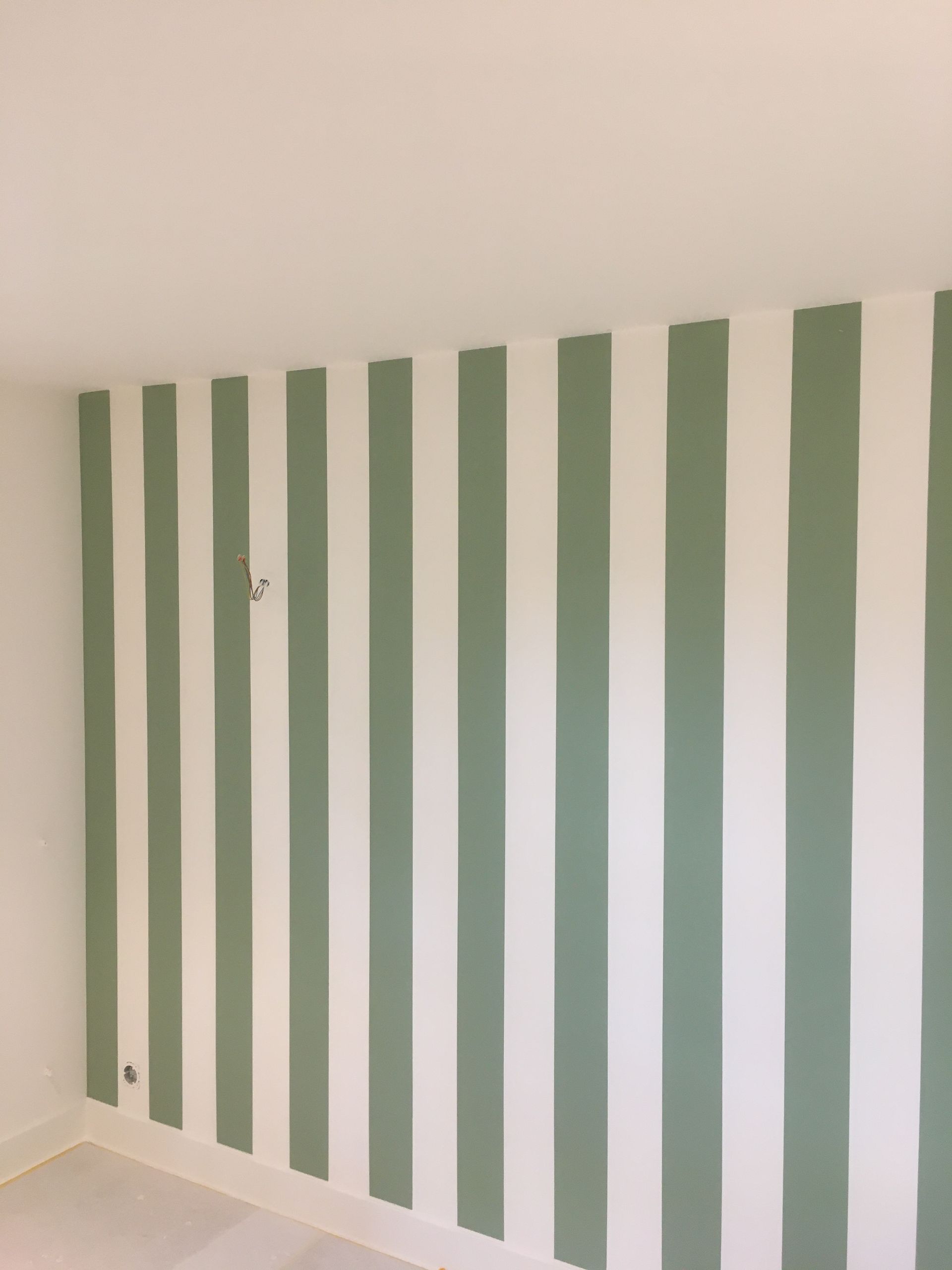 Mur blanc avec des rayures verticales vertes régulièrement espacées dans une pièce d'angle