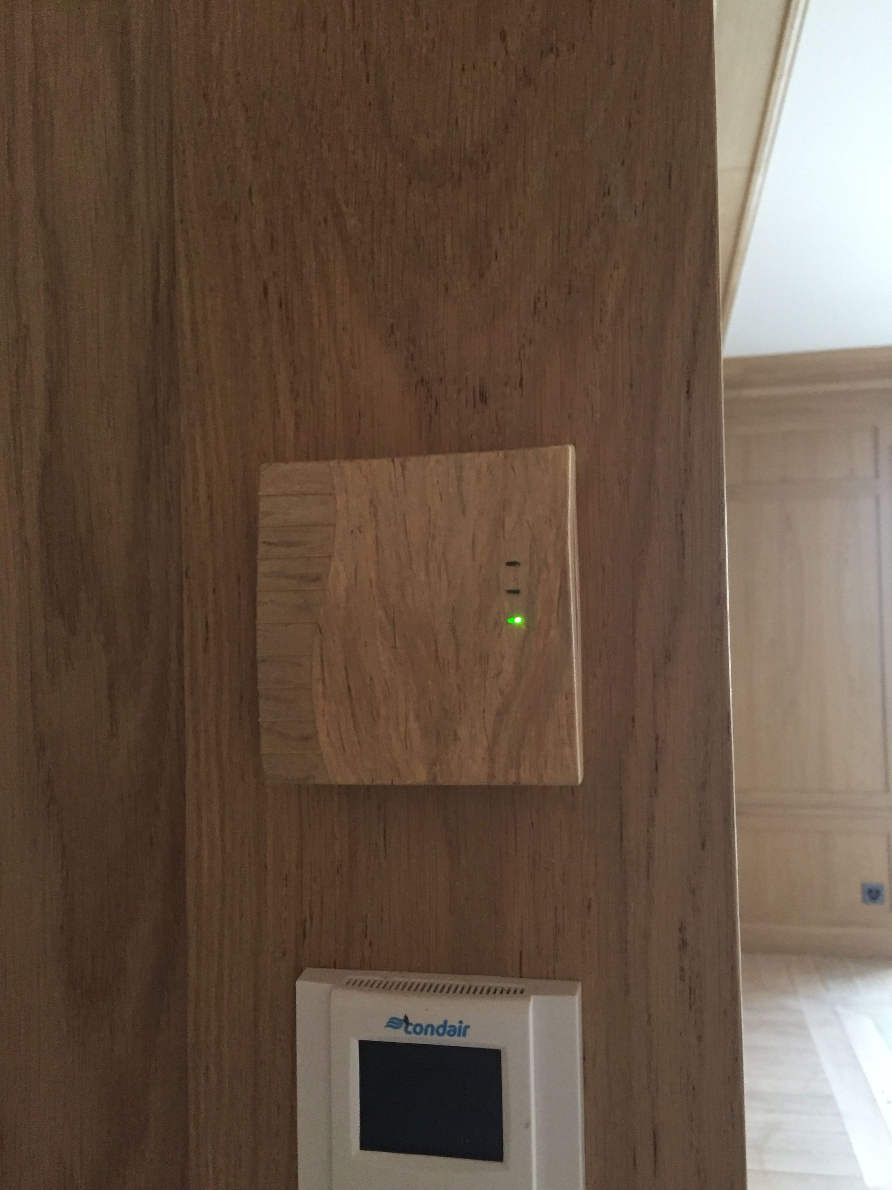 Panneau mural en bois avec un panneau carré et un voyant vert au-dessus d'un petit thermostat