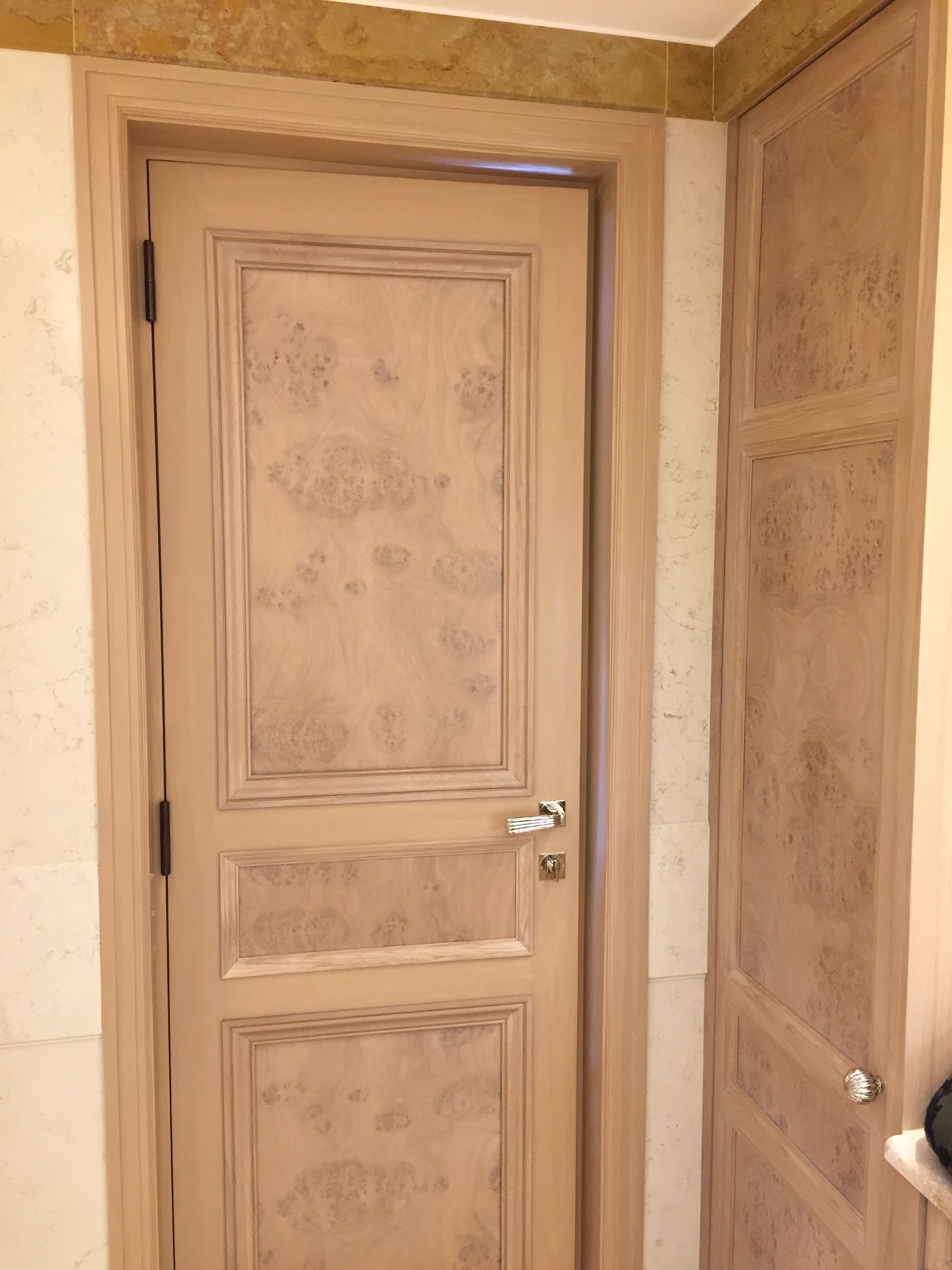 Porte intérieure en bois à panneaux dans un couloir beige, jouxtant des murs lambrissés assortis.