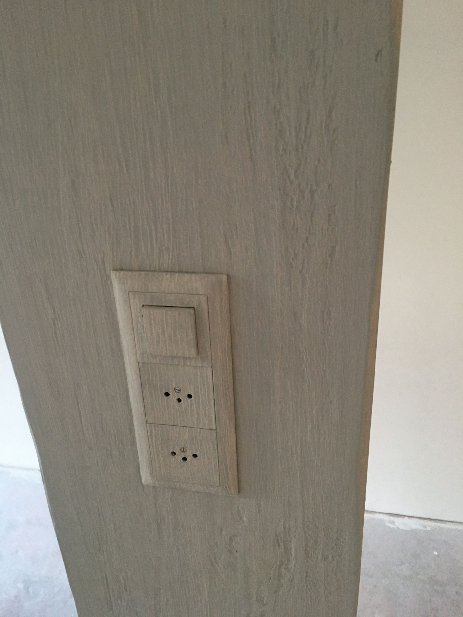 Plaque de prise électrique et d'interrupteur fixée au mur intérieur beige, près d'une porte.