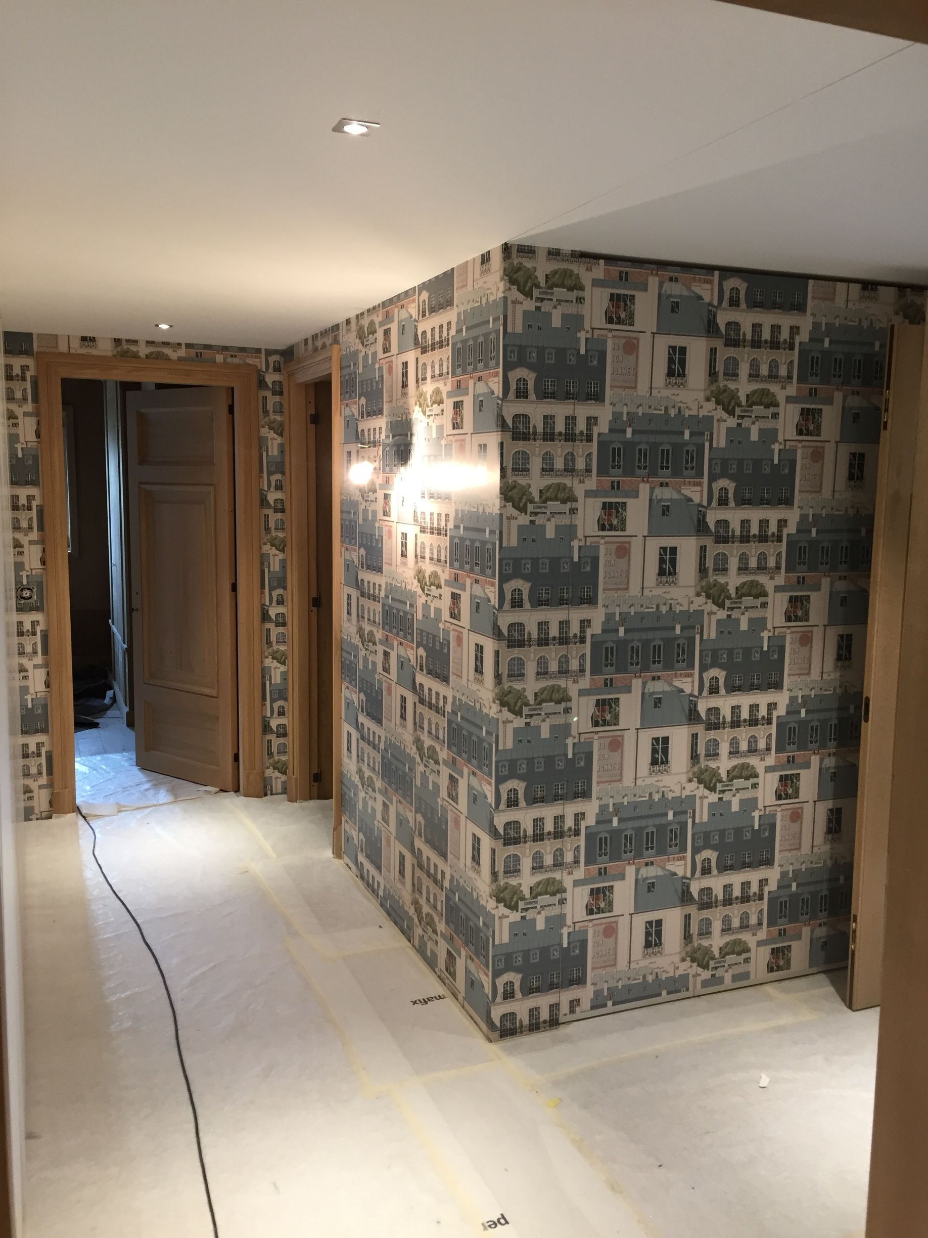 Couloir avec sol blanc, papier peint à motifs et spots encastrés au plafond ; porte visible au fond.