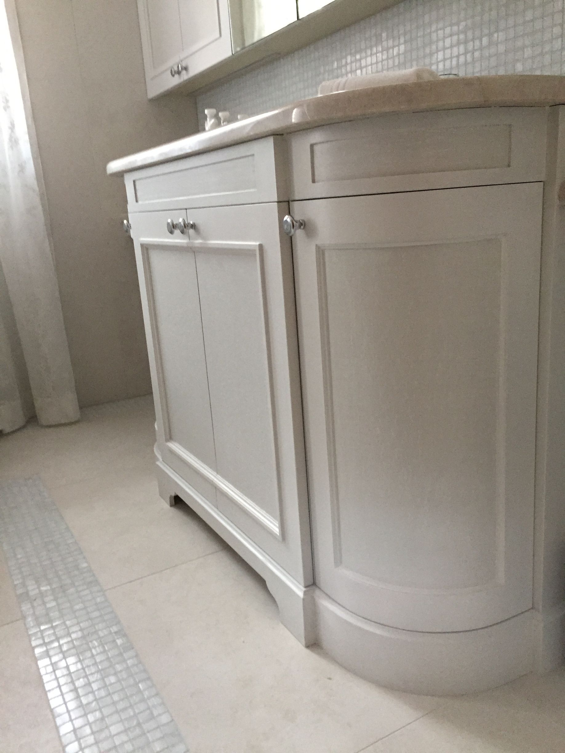 Meuble-lavabo blanc avec armoire incurvée et lavabo intégré, contre un sol et un mur carrelés.