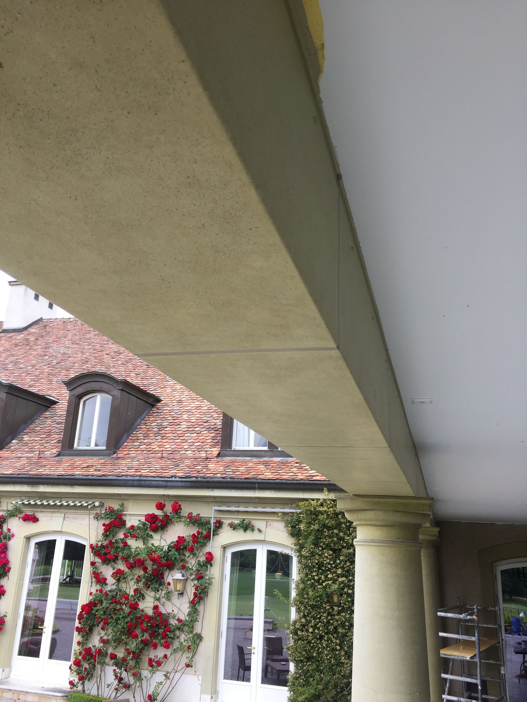 Vue d'une cour intérieure depuis un balcon, avec une maison aux tuiles rouges et des fenêtres recouvertes de lierre en arrière-plan.