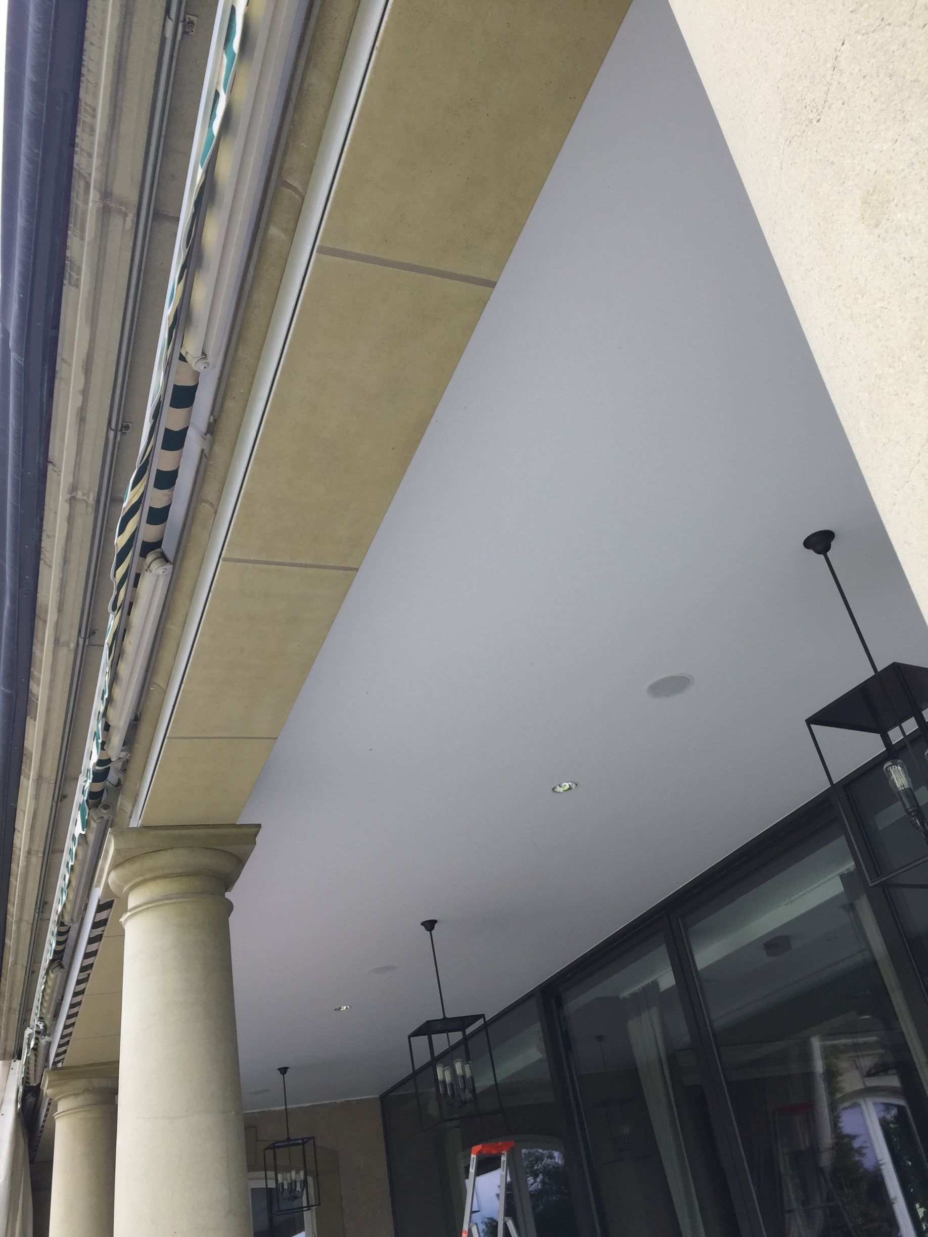 Allée extérieure couverte avec colonnes et luminaires suspendus à côté d'un bâtiment à façade vitrée