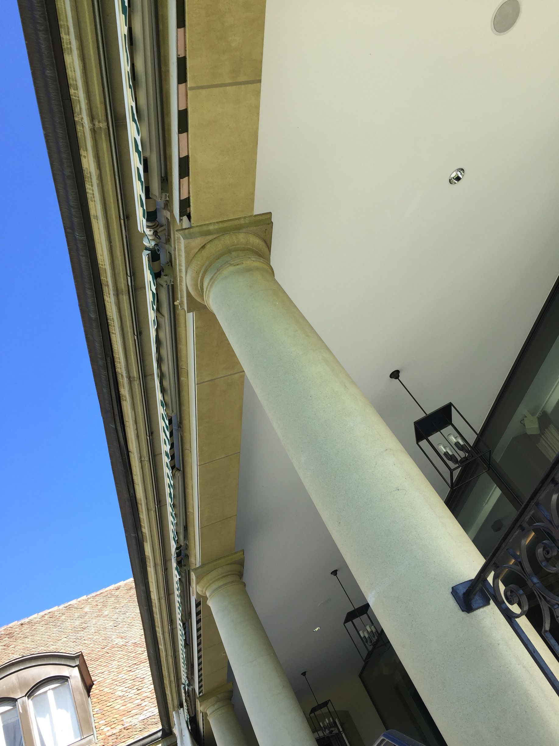 Vue plongeante sur le porche d'un bâtiment aux colonnes blanches, au plafond beige et au ciel bleu.