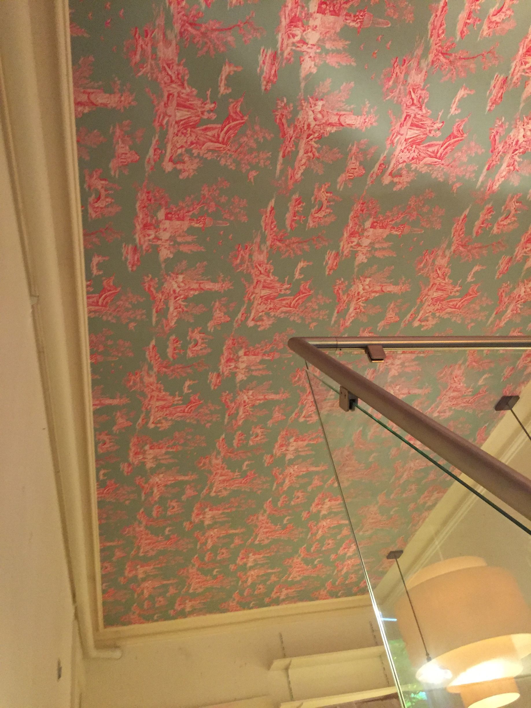 Plafond recouvert de papier peint texturé rose au-dessus d'une rampe d'escalier et d'un luminaire en verre