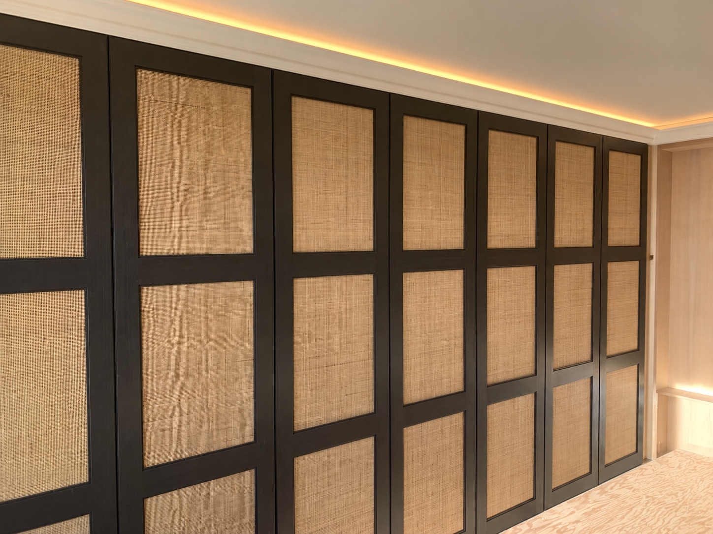 Mur de panneaux tissés encadrés de bois sombre dans une pièce moderne à l'éclairage chaleureux, avec éclairage indirect LED au-dessus