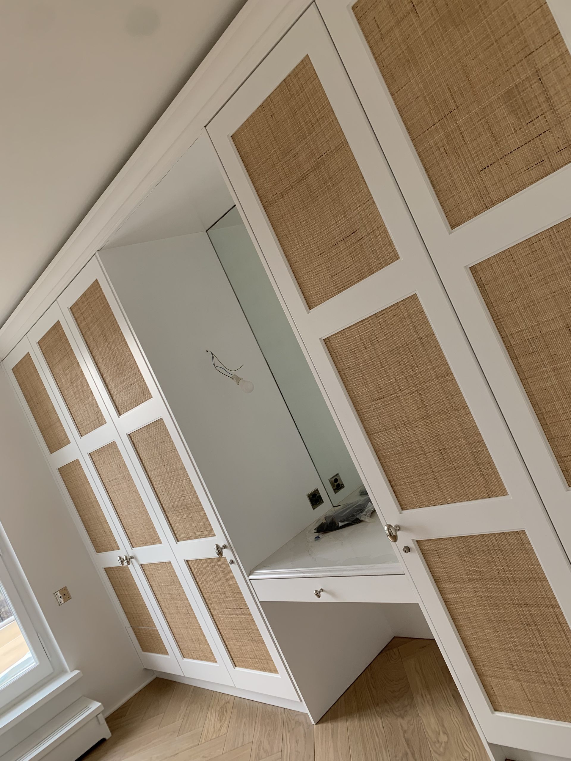 Armoire encastrée blanche avec portes à panneaux tissés et petite coiffeuse dans une chambre lumineuse.