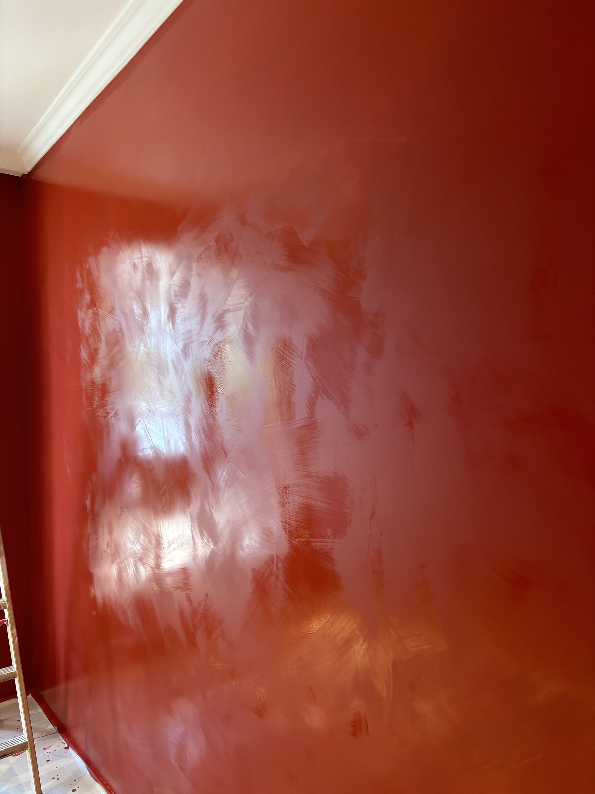 Un mur peint en rouge avec des reflets brillants et un coin de plafond blanc.