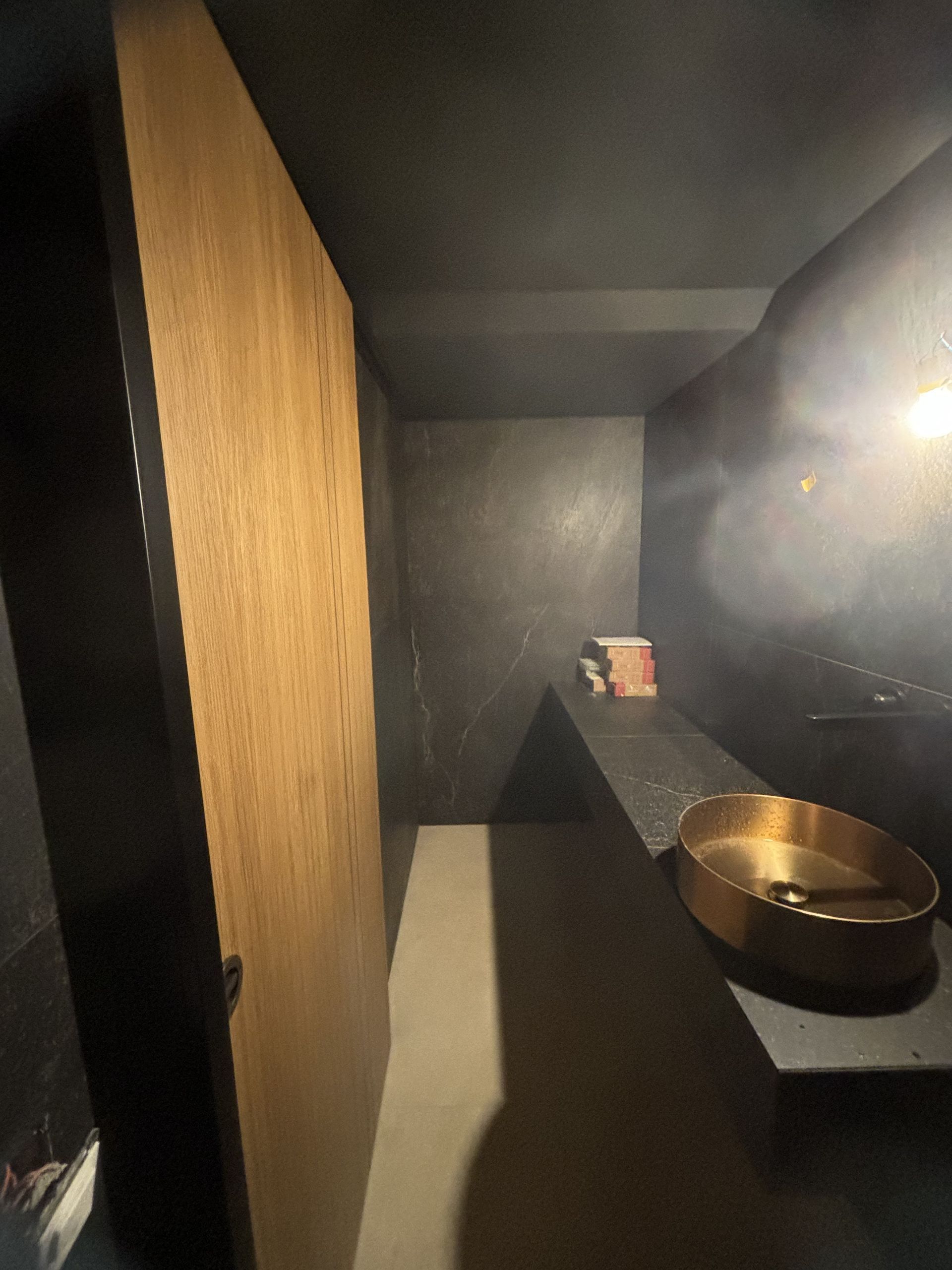 Toilettes modernes à l'éclairage tamisé, avec une cabine en bois, des murs gris et un lavabo en cuivre éclairé par une lumière vive.