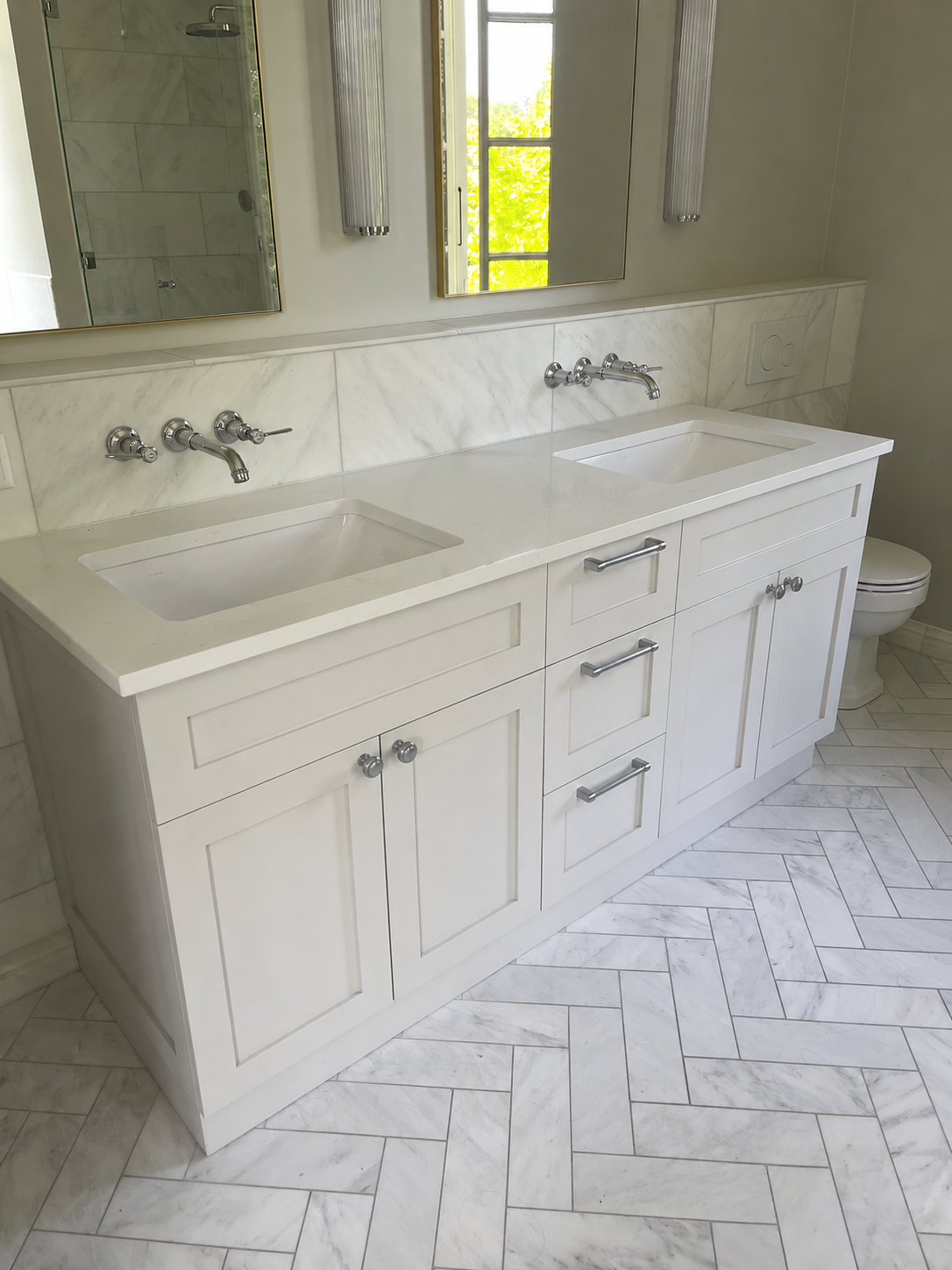 Meuble-lavabo double vasque blanc avec comptoir en marbre, robinetterie chromée et miroir au-dessus, dans une salle de bain carrelée et lumineuse