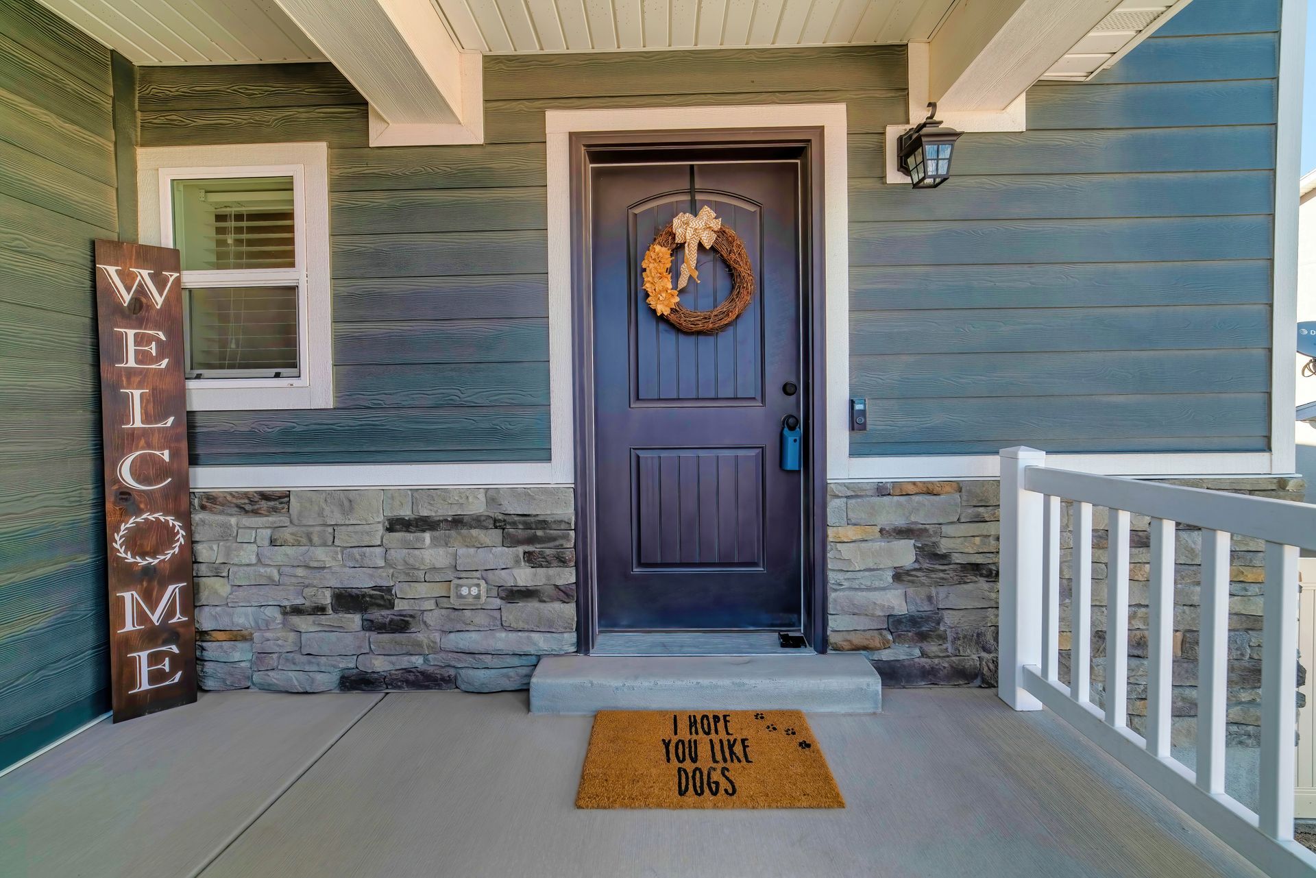 Front porch with blue siding, white trim, wreath on door, welcome sign, and doormat. Front porch with blue siding, white trim, wreath on door, welcome sign, and doormat.