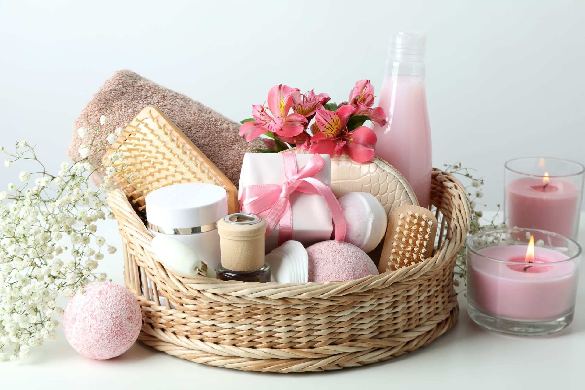 Spa gift basket with pink bath items, flowers, candles, and a bottle on a white background Spa gift basket with pink bath items, flowers, candles, and a bottle on a white background