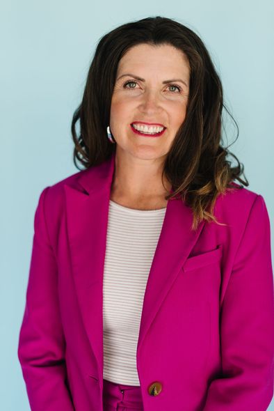 Woman in a bright magenta blazer smiling against a light blue background