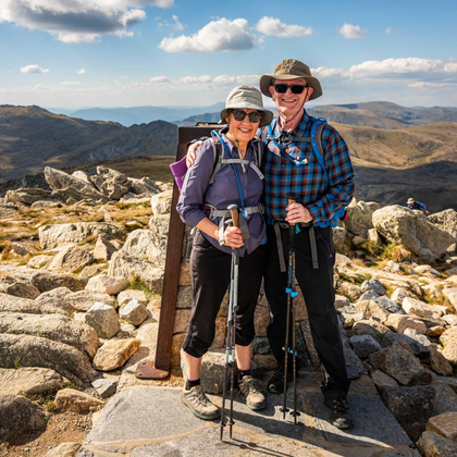 Happy couple with trekking poles standing on a rocky mountain summit under a blue sky