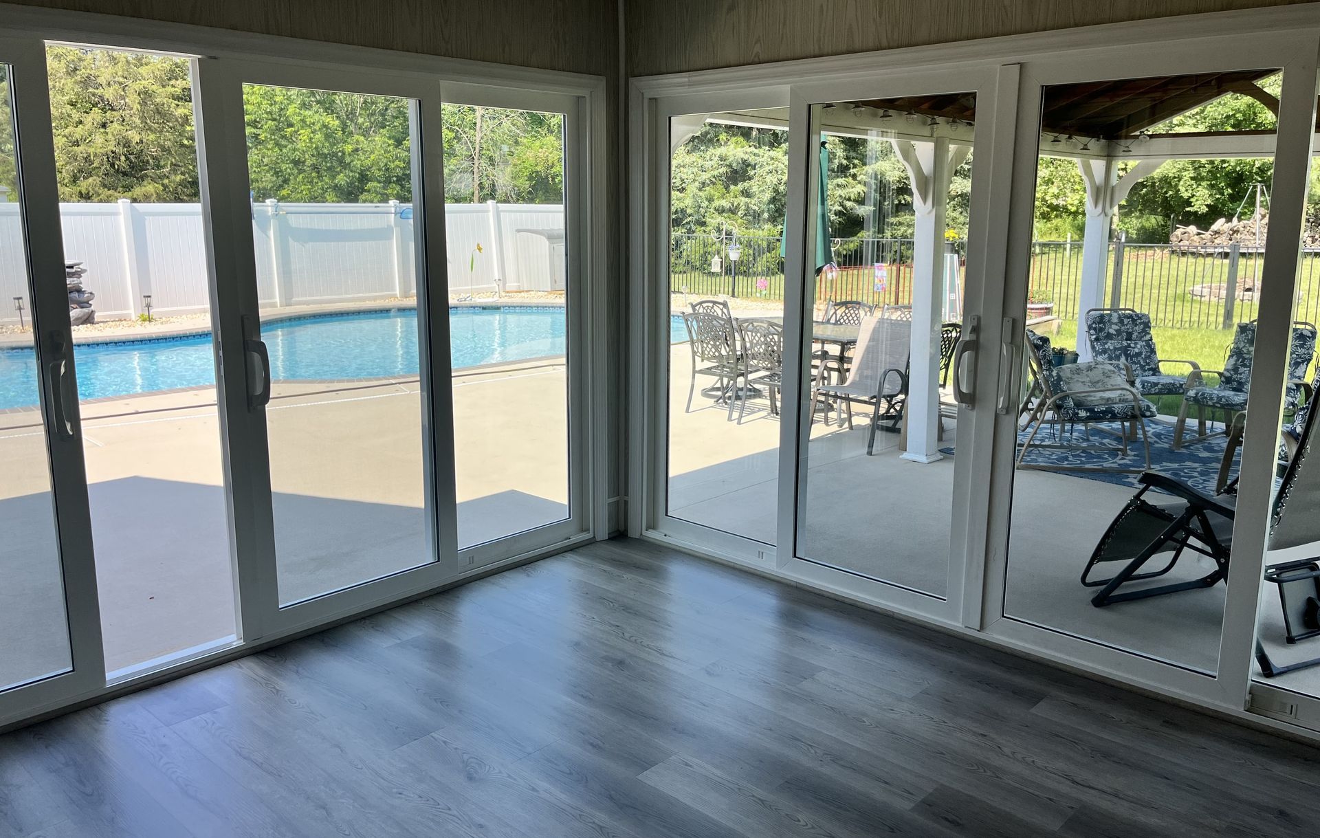 Empty room with large windows overlooking a backyard pool and patio furniture