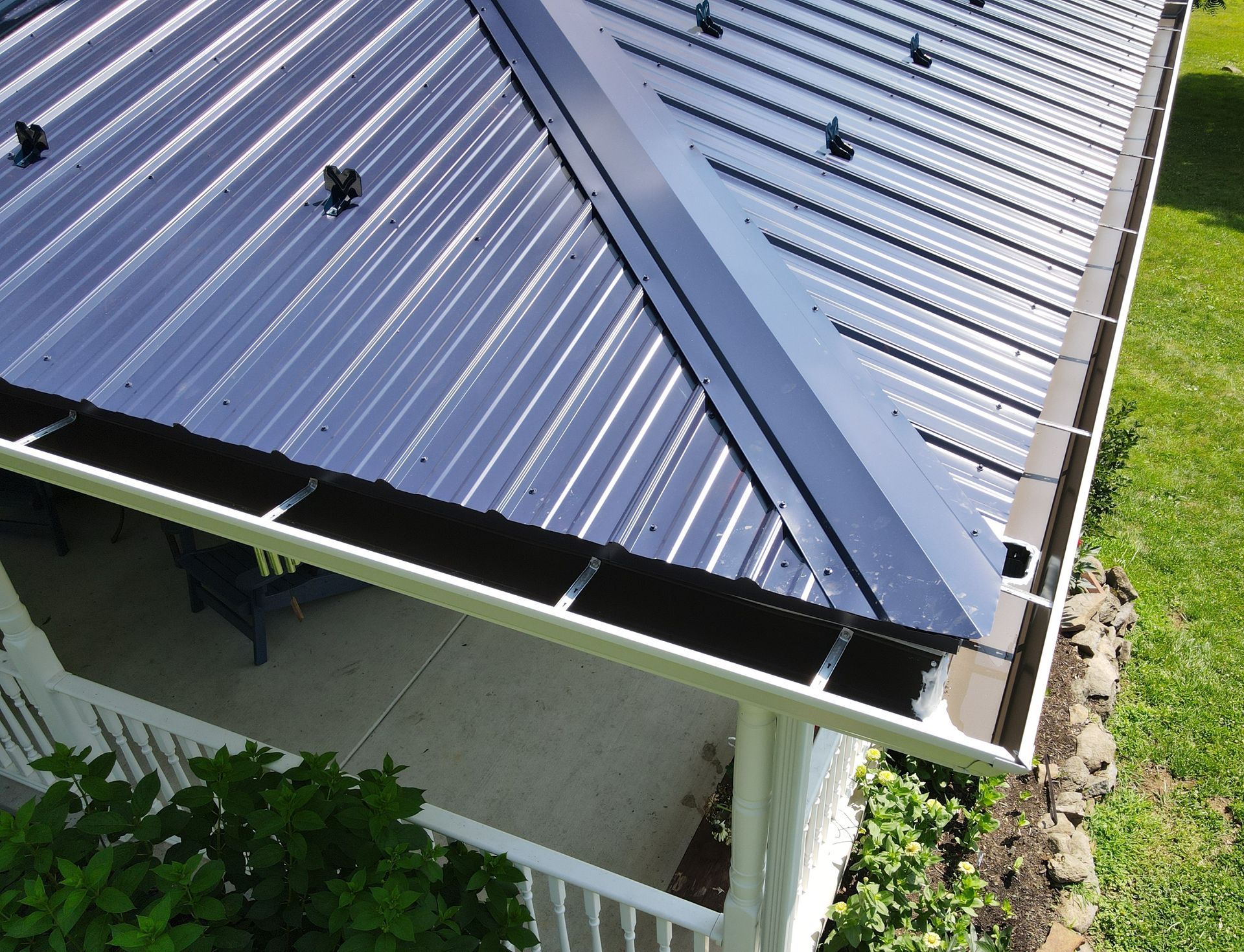 Blue metal roof with damaged edge above a white porch and green lawn below