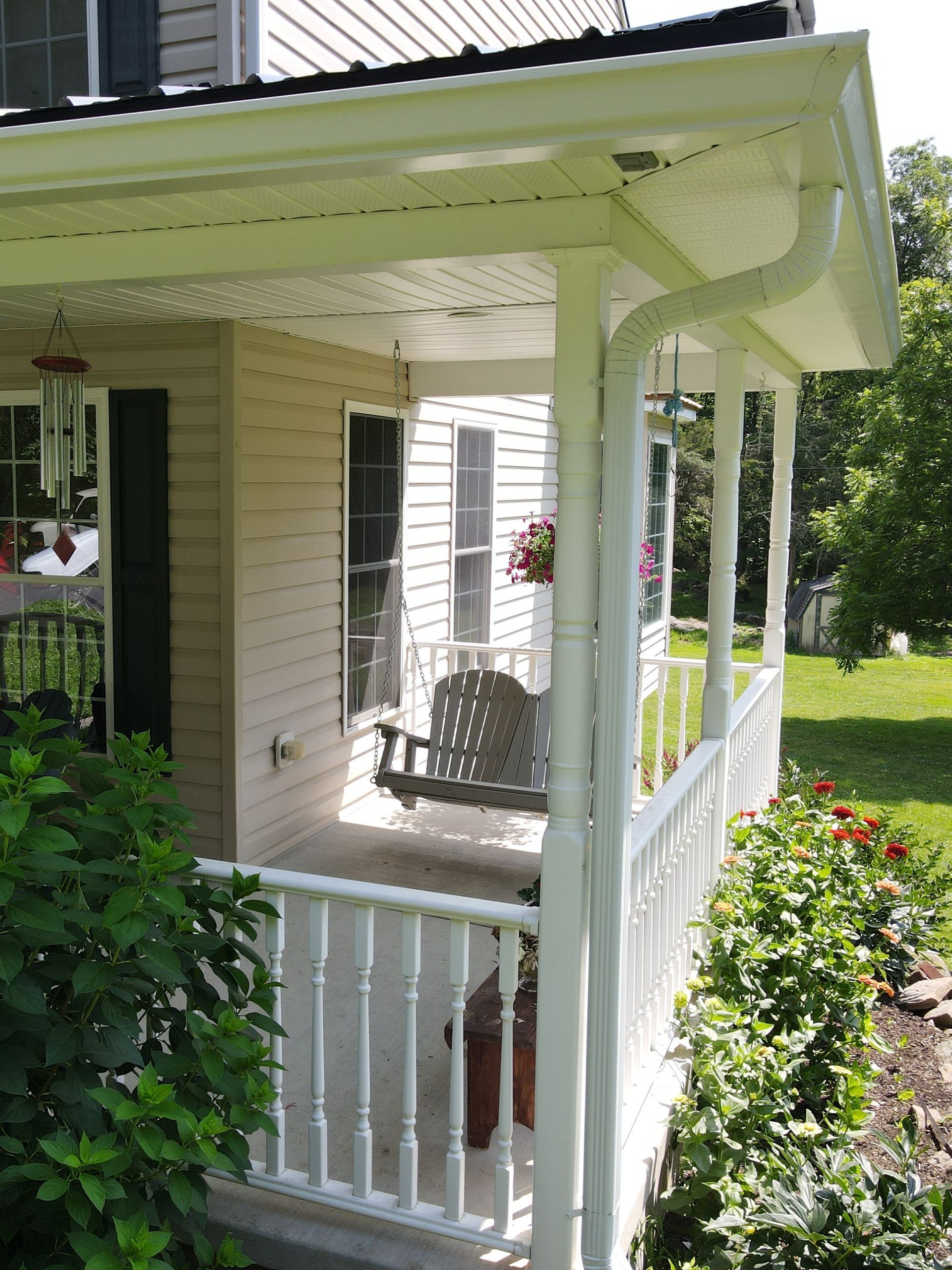 White front porch with railing, rocking chair, and hanging plant beside a house and garden path