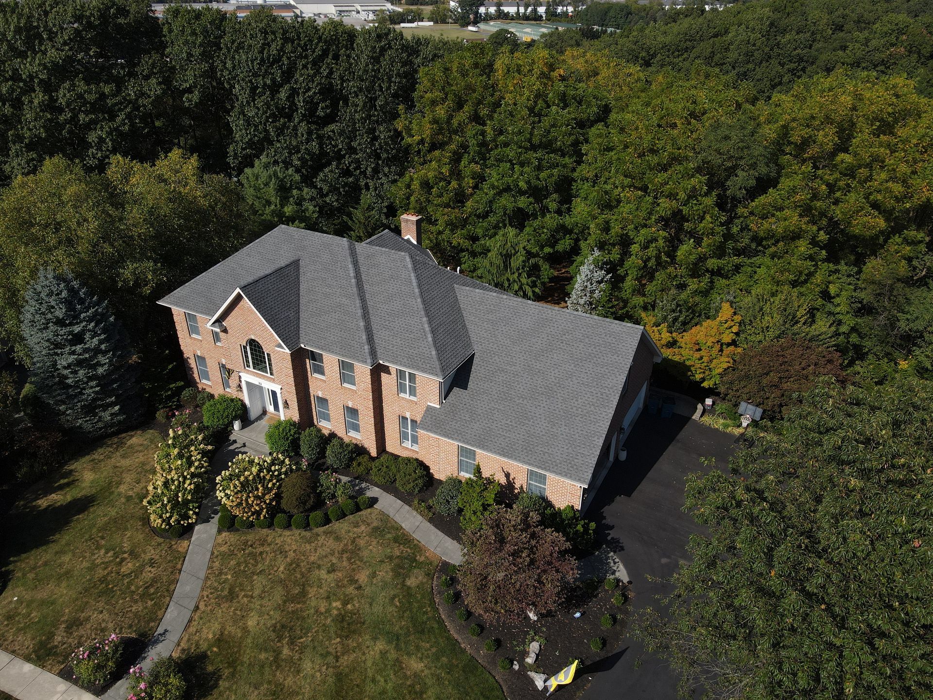Aerial view of a brick house with a dark roof, surrounded by trees and a grassy yard