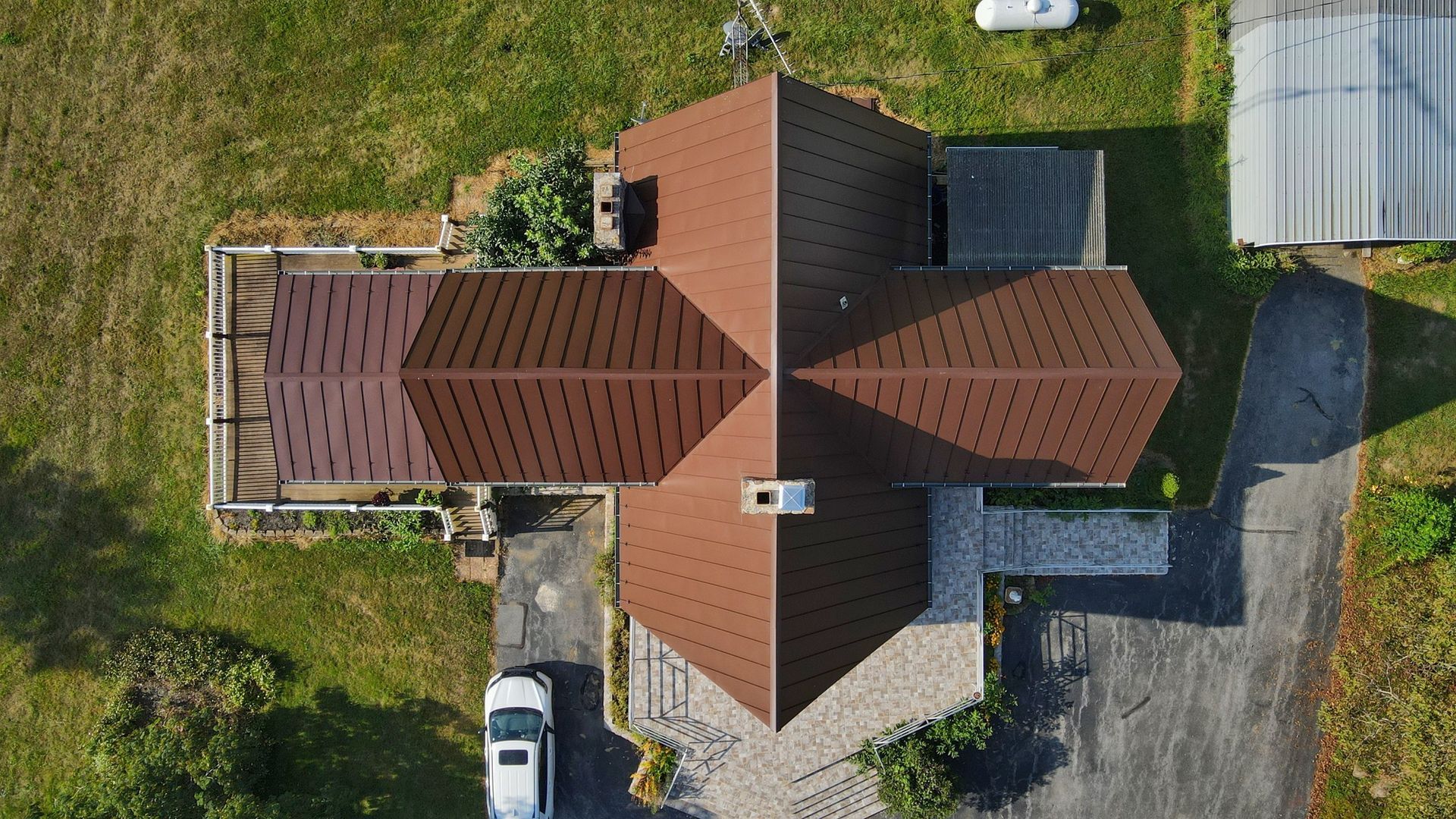 Top-down view of a house with a brown roof, surrounded by grass, driveway, and parked vehicles.
