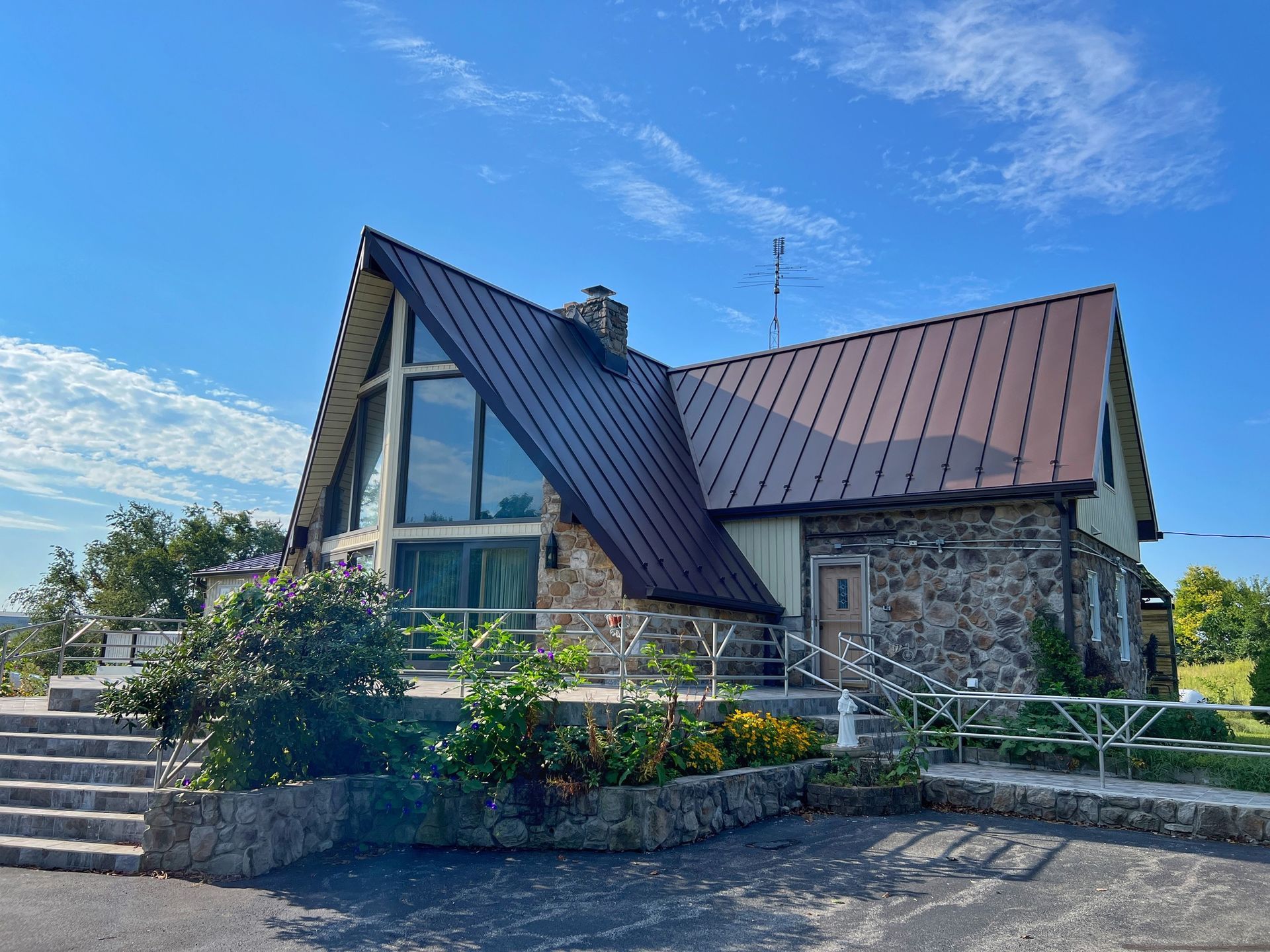 Stone chapel with steep red roof and blue sky, viewed from a landscaped entrance with steps and railing