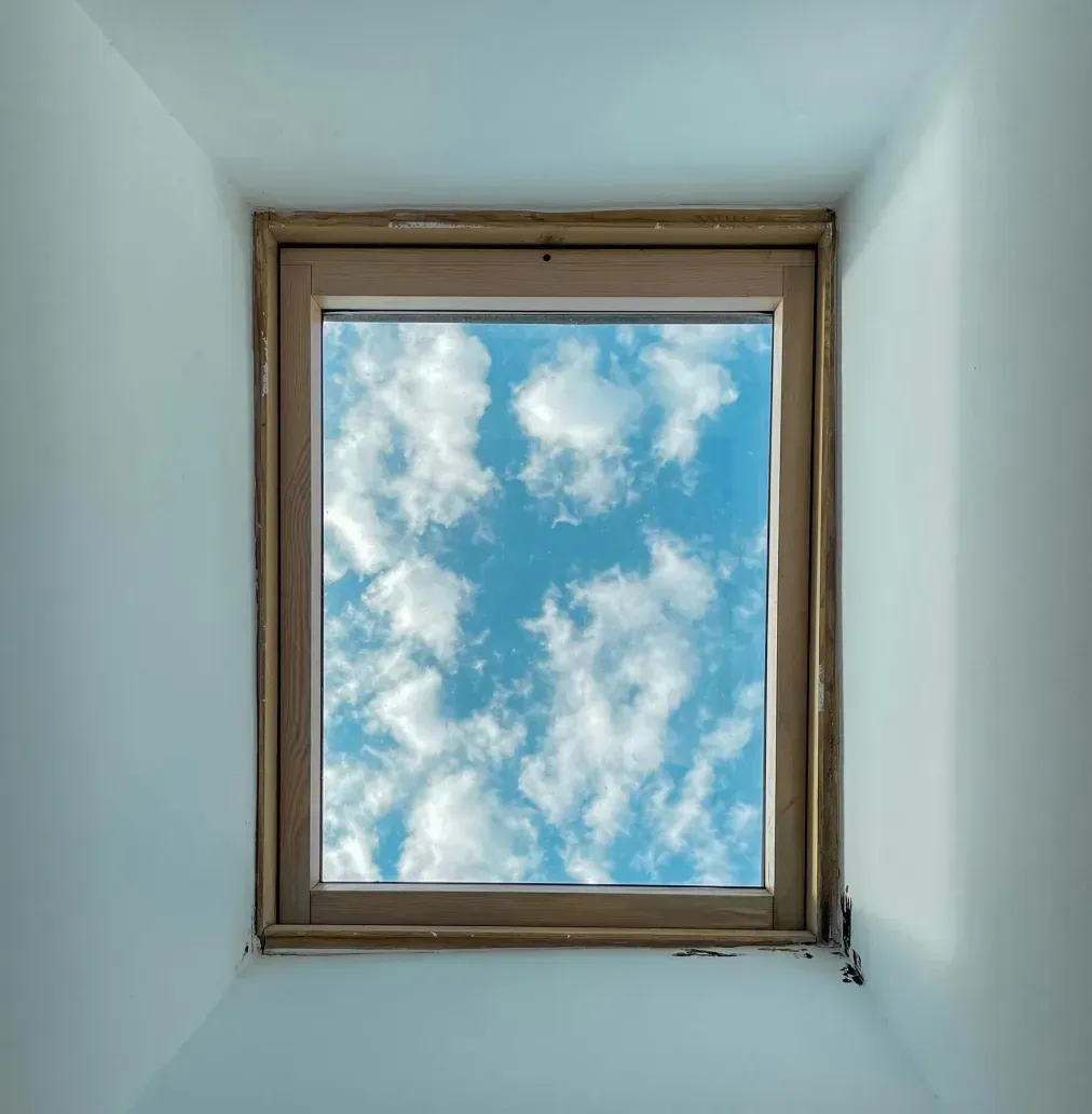 View up through a skylight window framing blue sky and white clouds