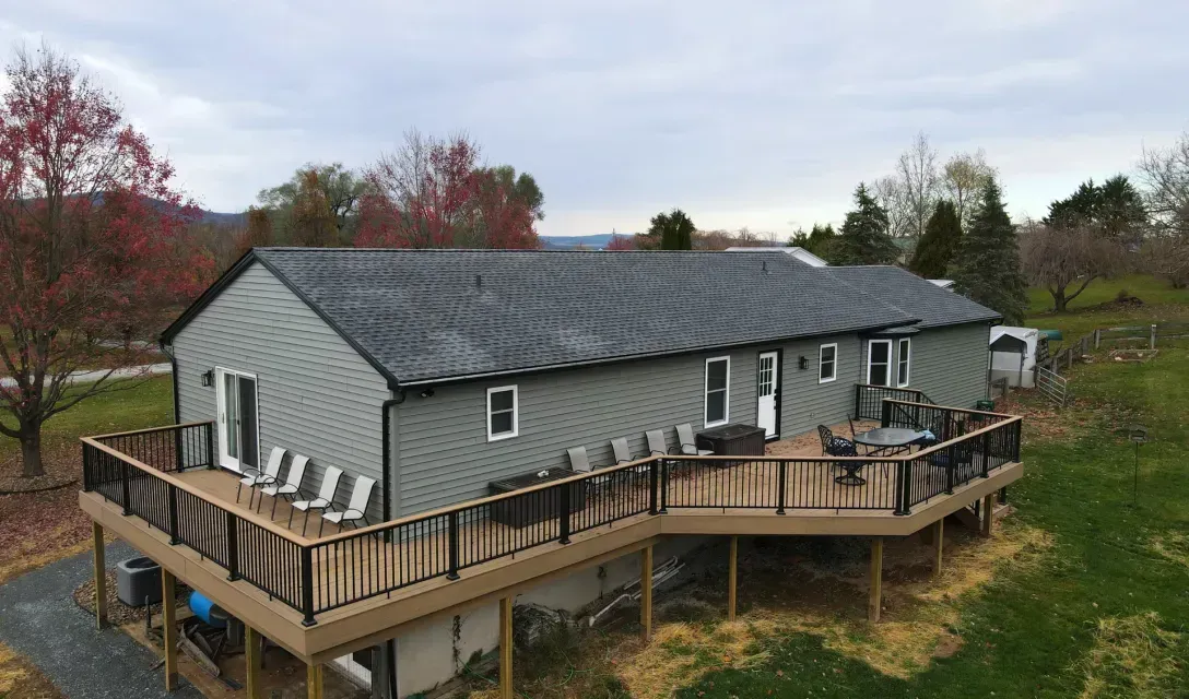 An image of a home with a gray roof, muted green siding, and a custom wrap-around second-story deck by Dayhoff Construction.